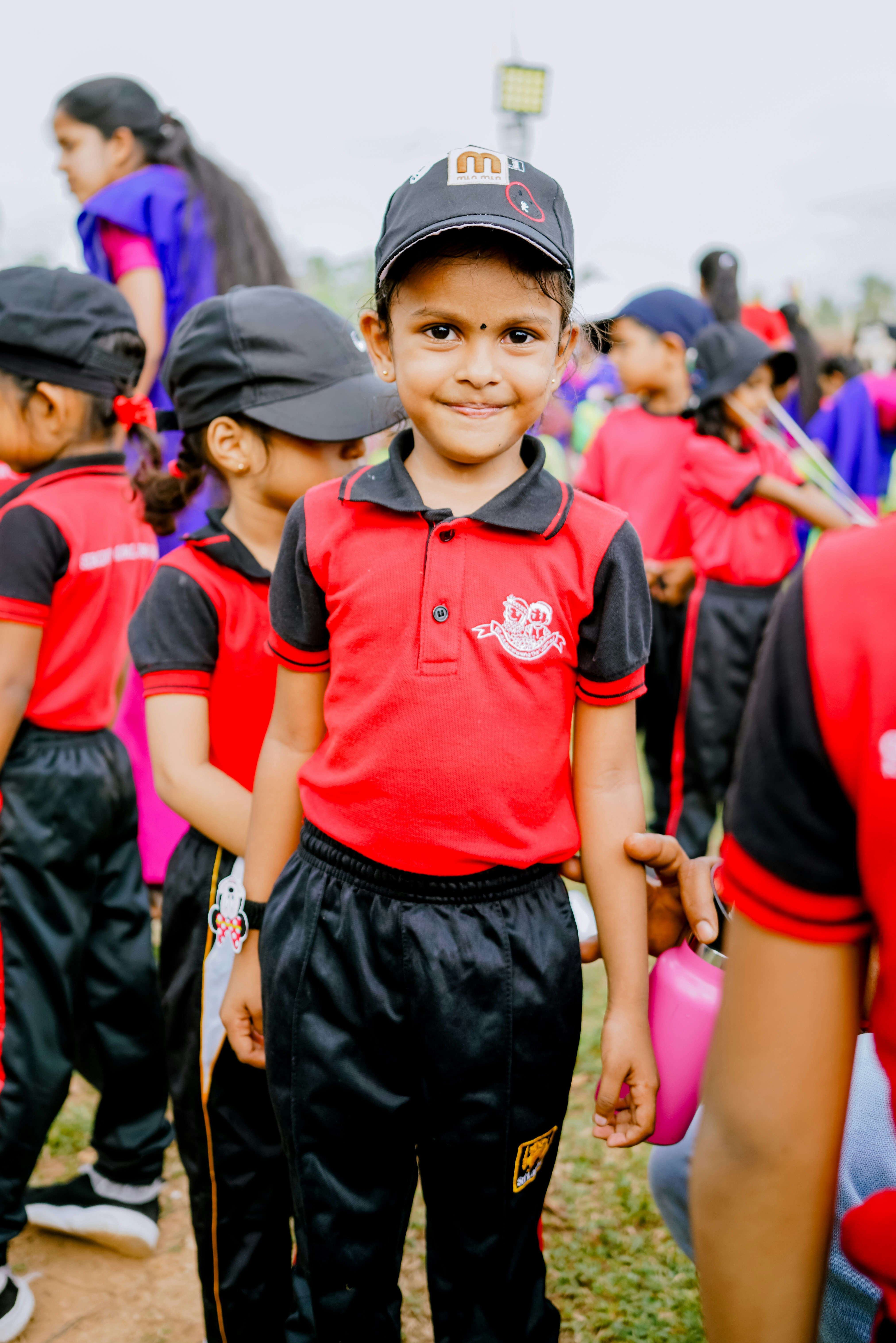 A young girl in a red and black uniform and cap standing outdoors