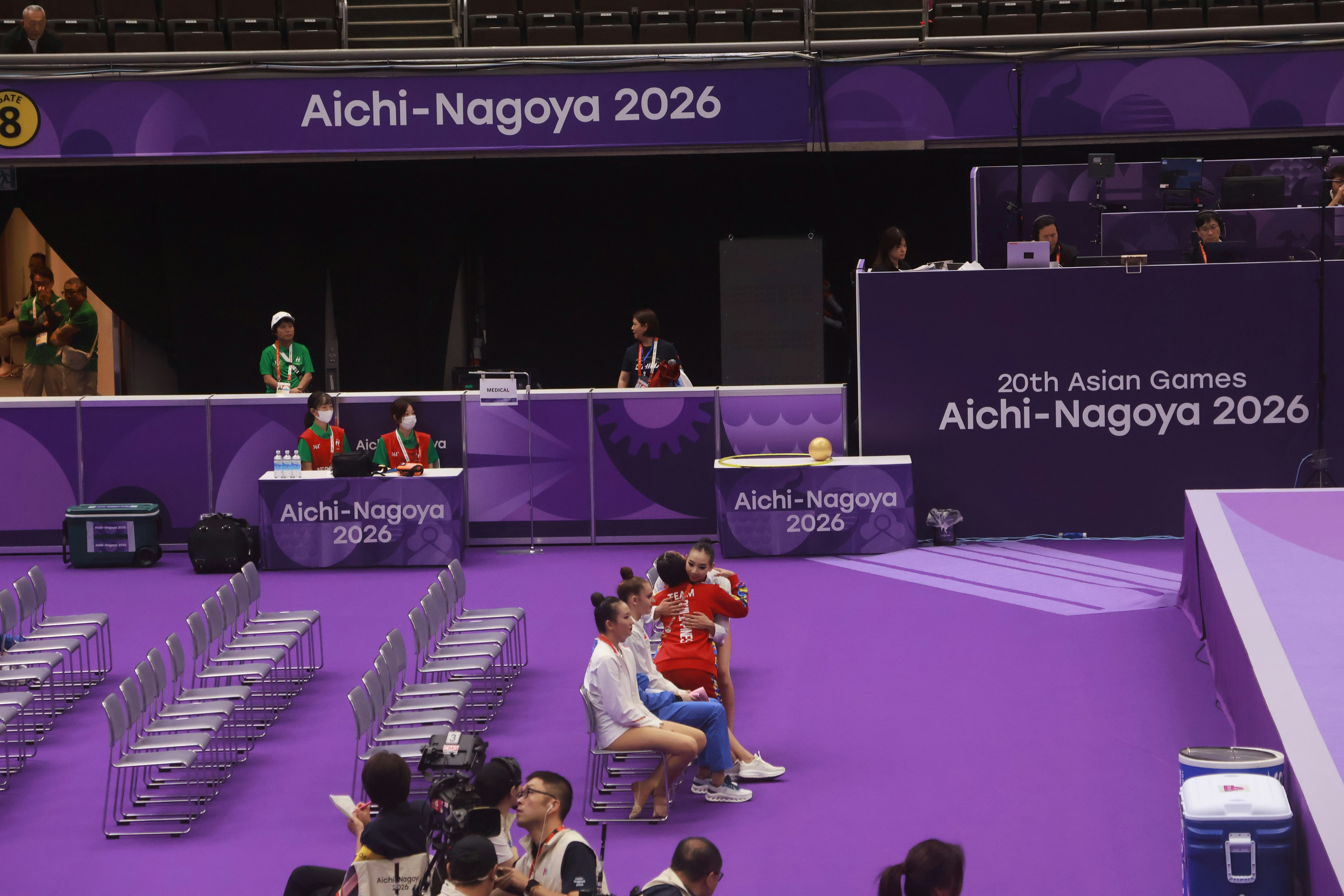 Gymnasts hugging on chairs in a purple arena at the Asian Games