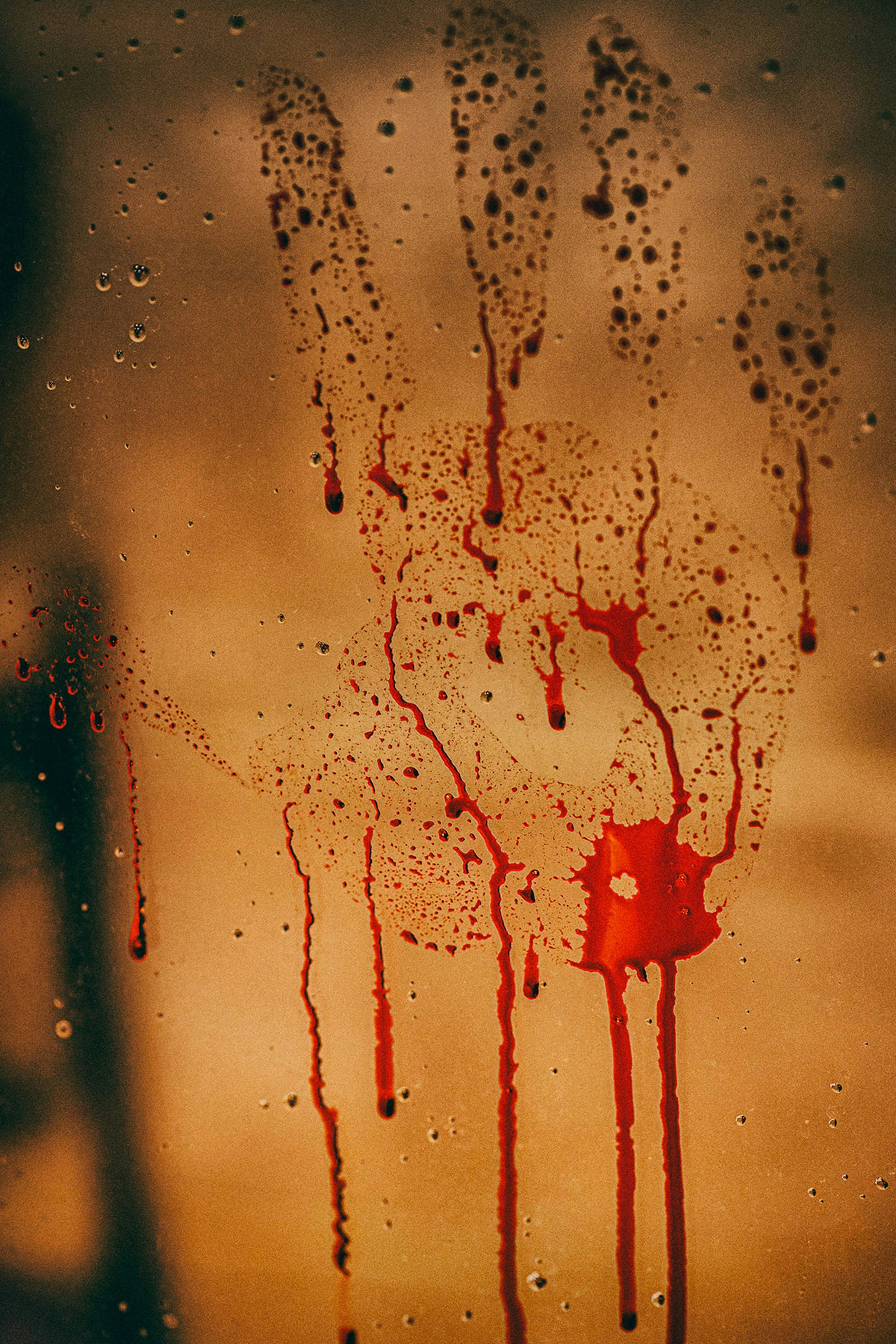 A red handprint with dripping liquid on a glass surface against a warm background