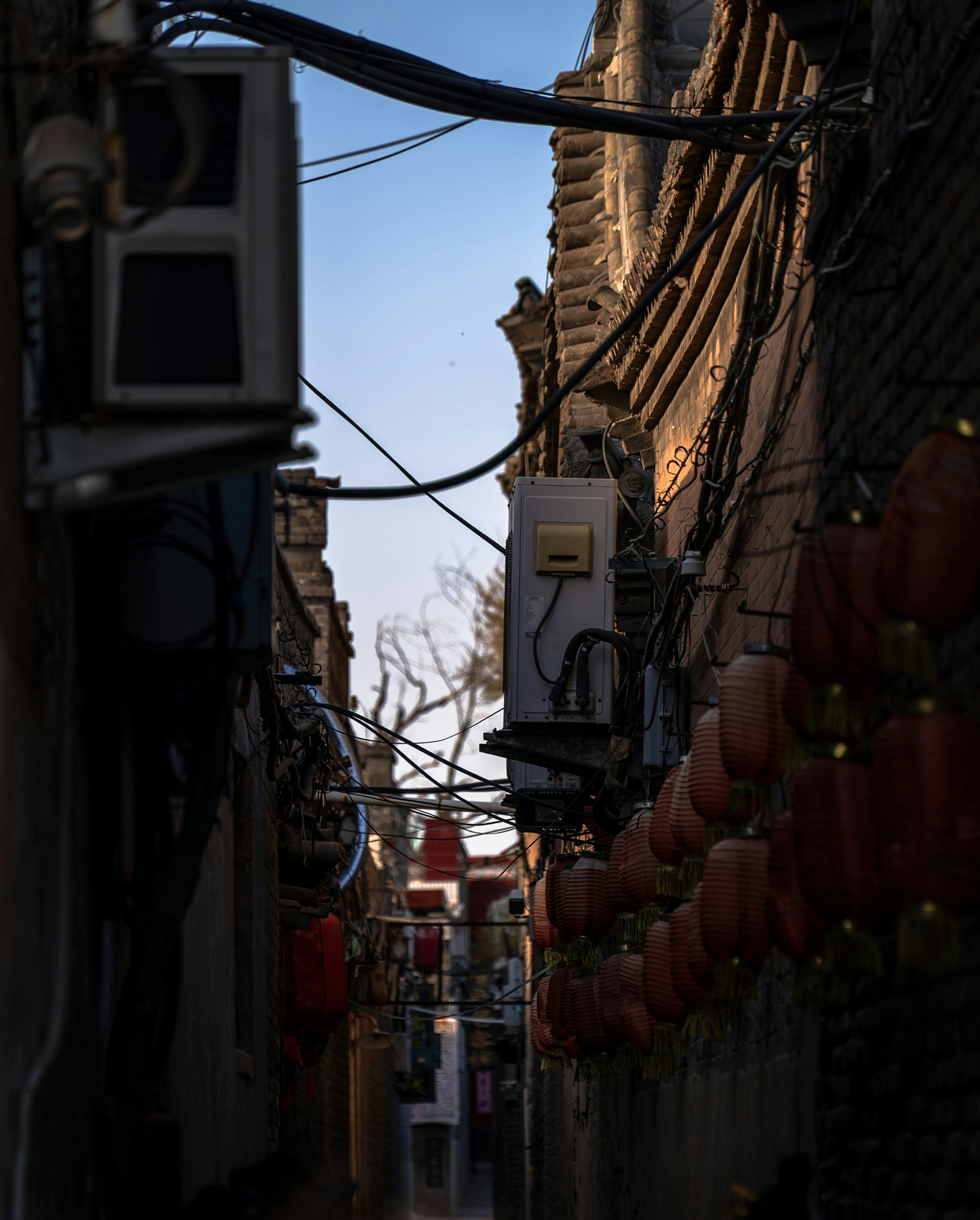 Red lanterns hanging along a narrow brick alleyway with overhead electrical wires