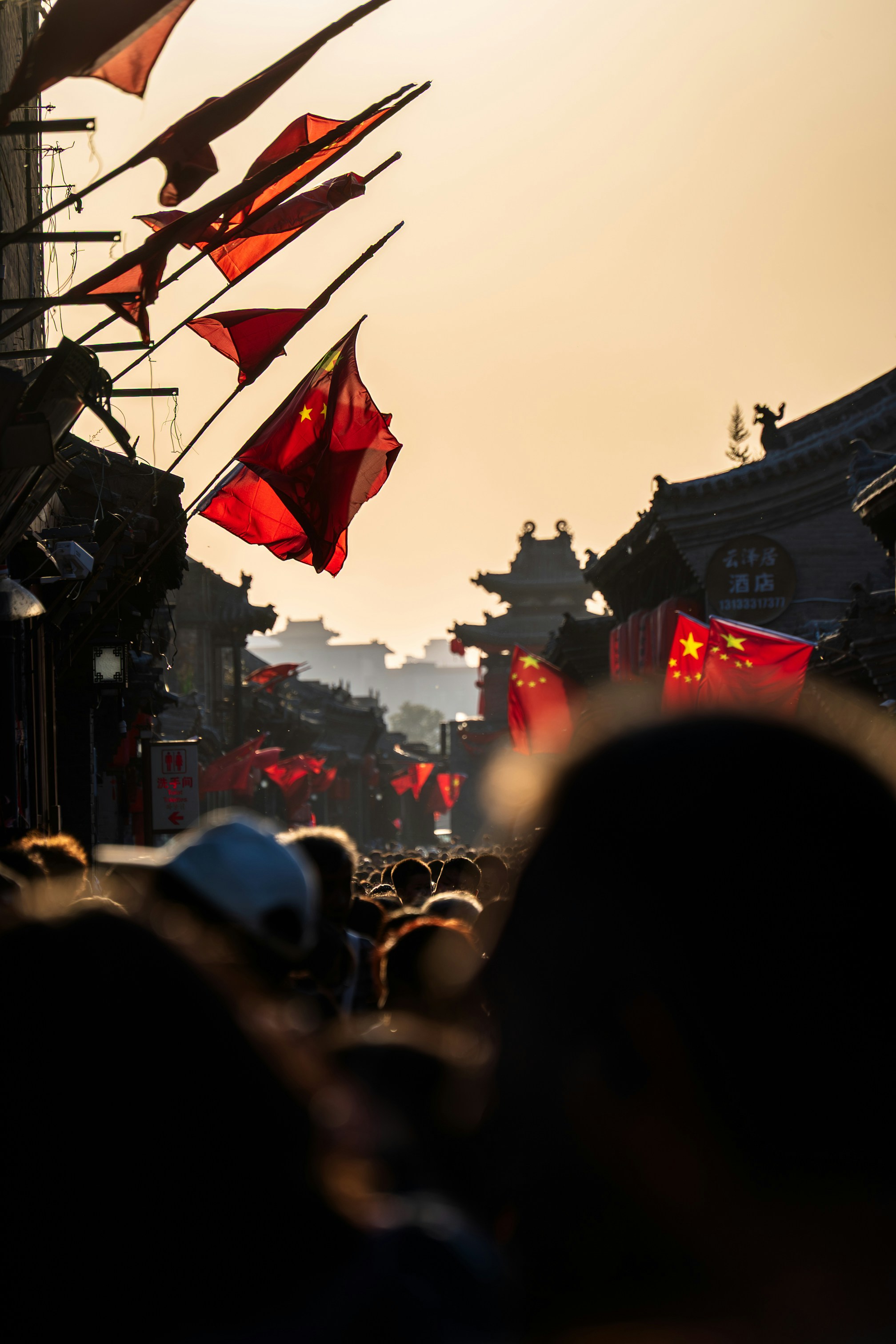 Red flags with yellow stars lining a crowded street under a warm golden sky