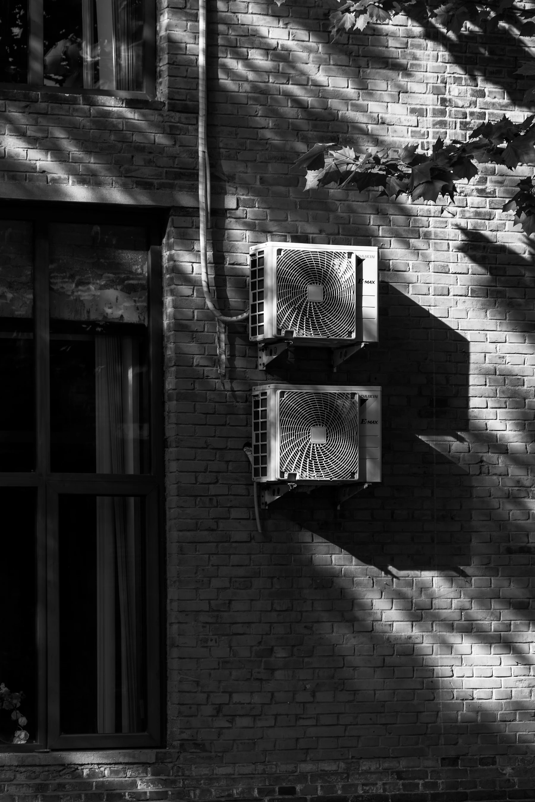 Two air conditioning condenser units mounted on a sunlit brick wall