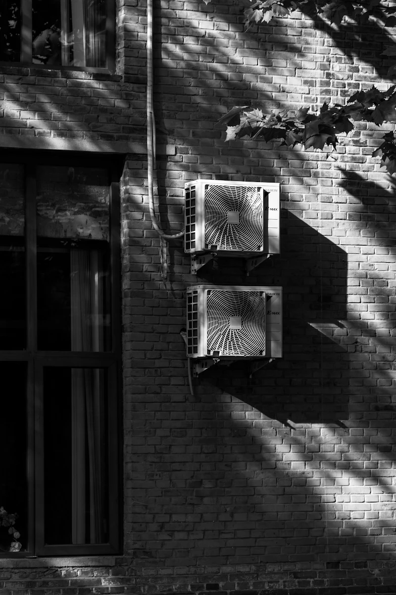 Two air conditioning condenser units mounted on a sunlit brick wall