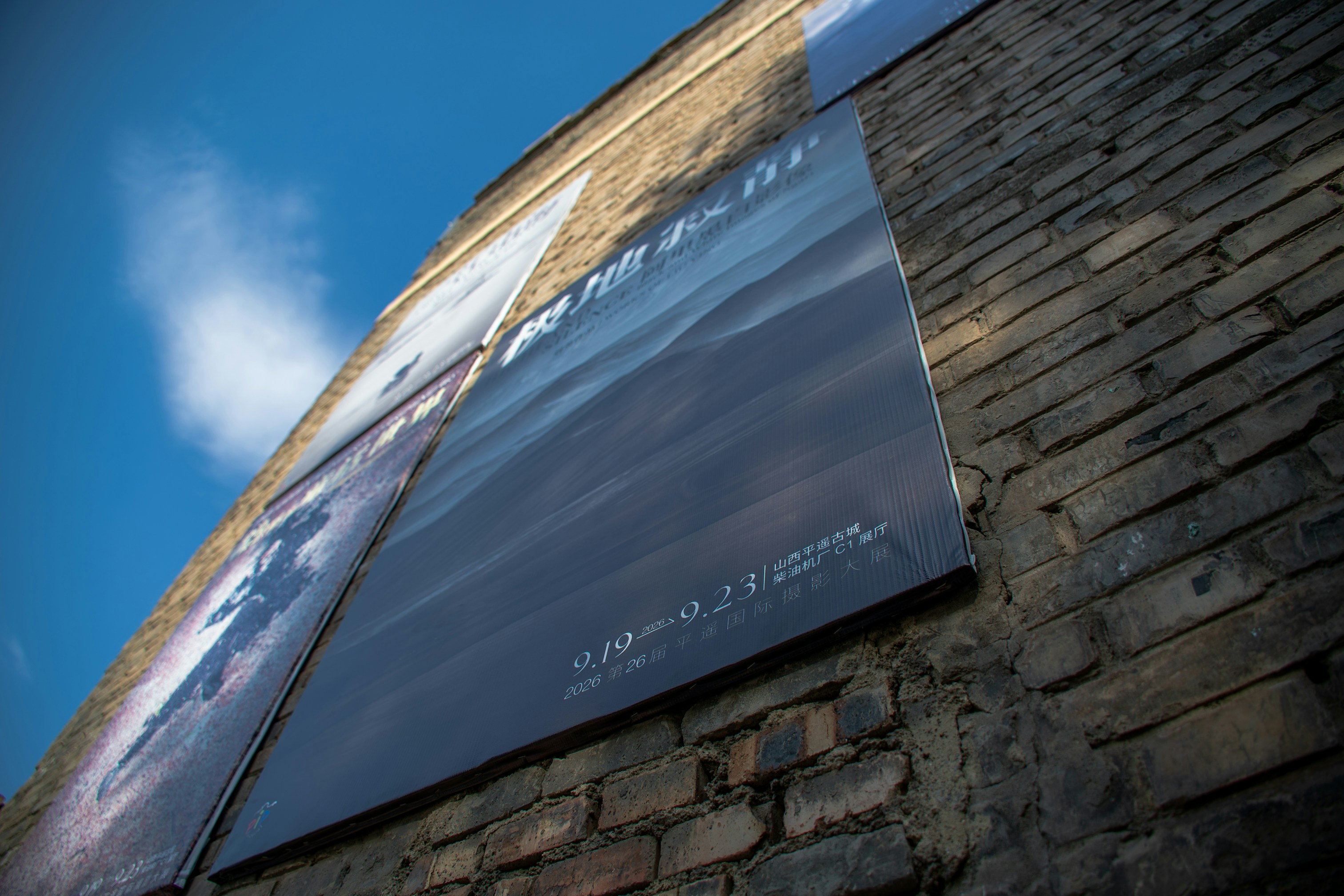 Large posters mounted on a weathered brick wall under a bright blue sky