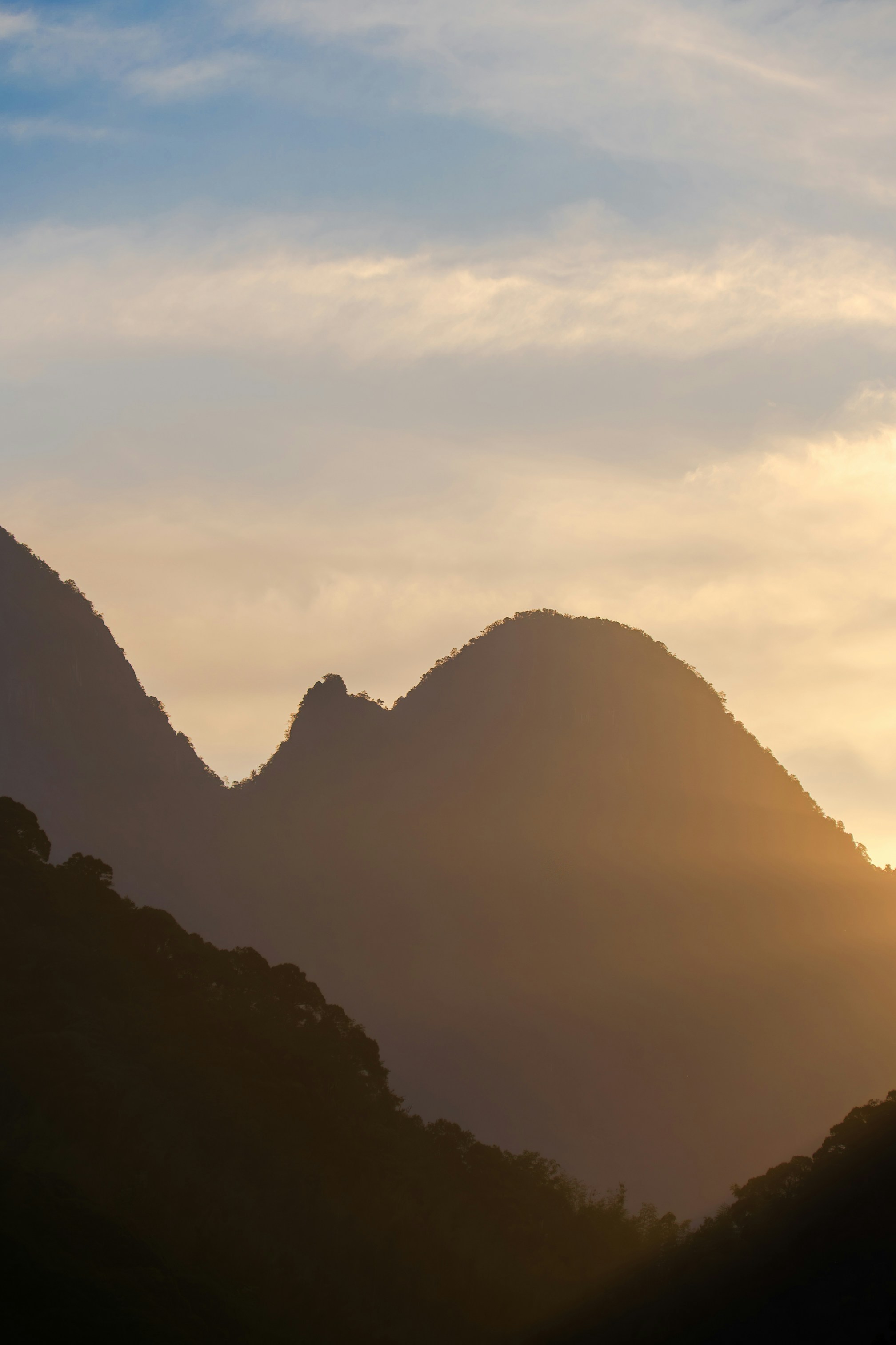 Silhouetted mountain peaks against a soft golden hour sky with light clouds
