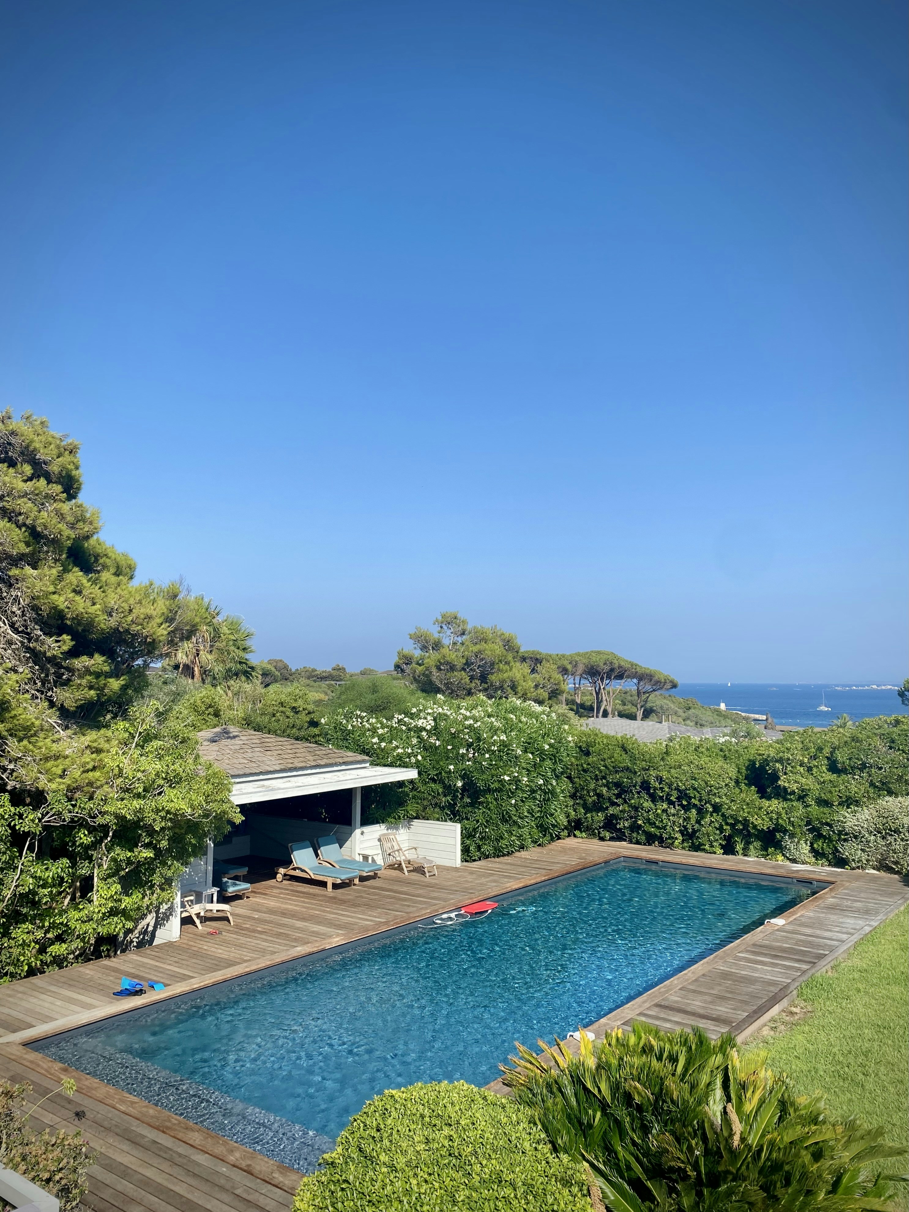 A rectangular swimming pool with a wooden deck and lounge chairs near the sea