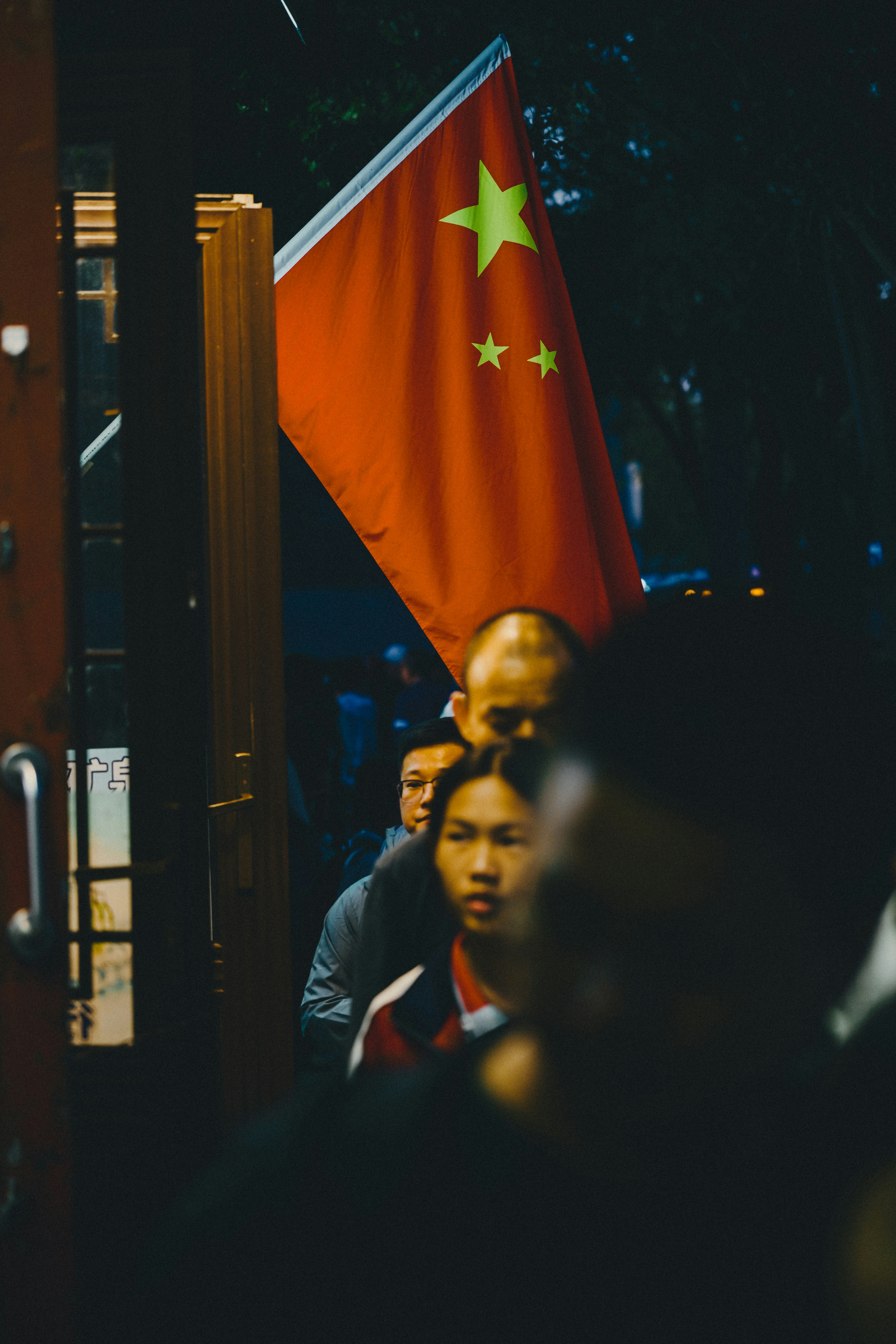 People walking past a red flag of China at night