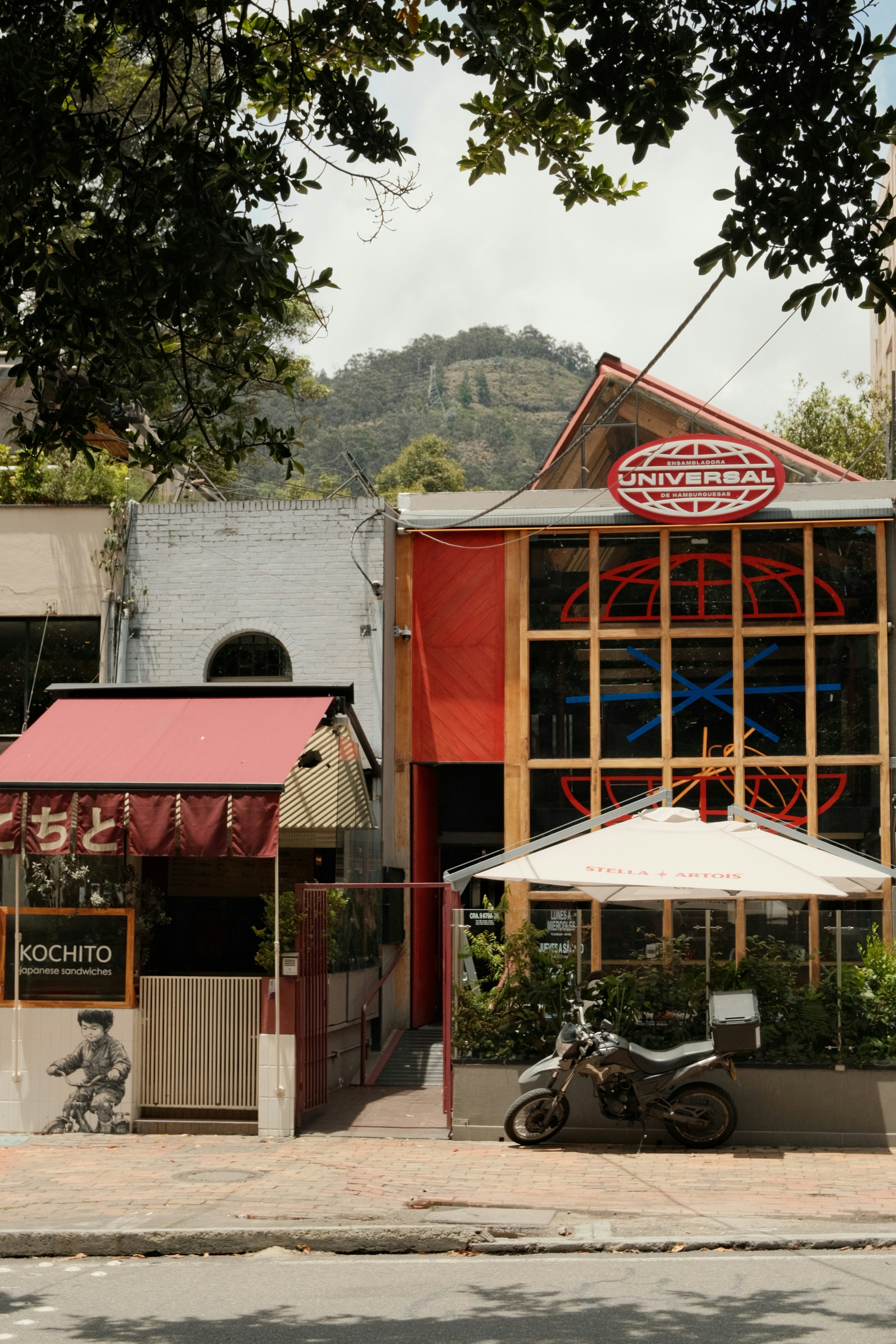 A street view of a restaurant with a red awning and a motorcycle parked outside