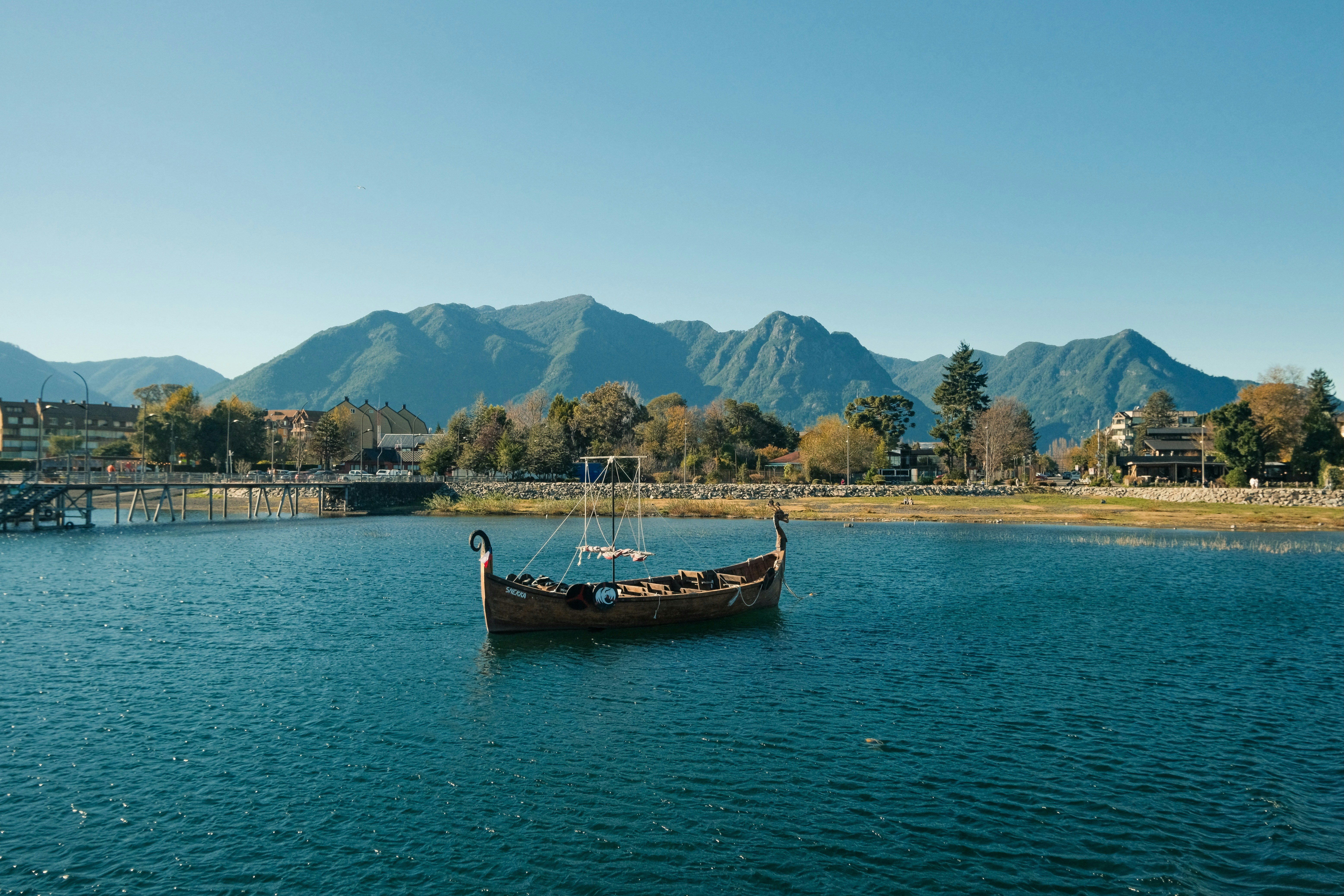 A wooden Viking ship on a blue lake before distant green mountains