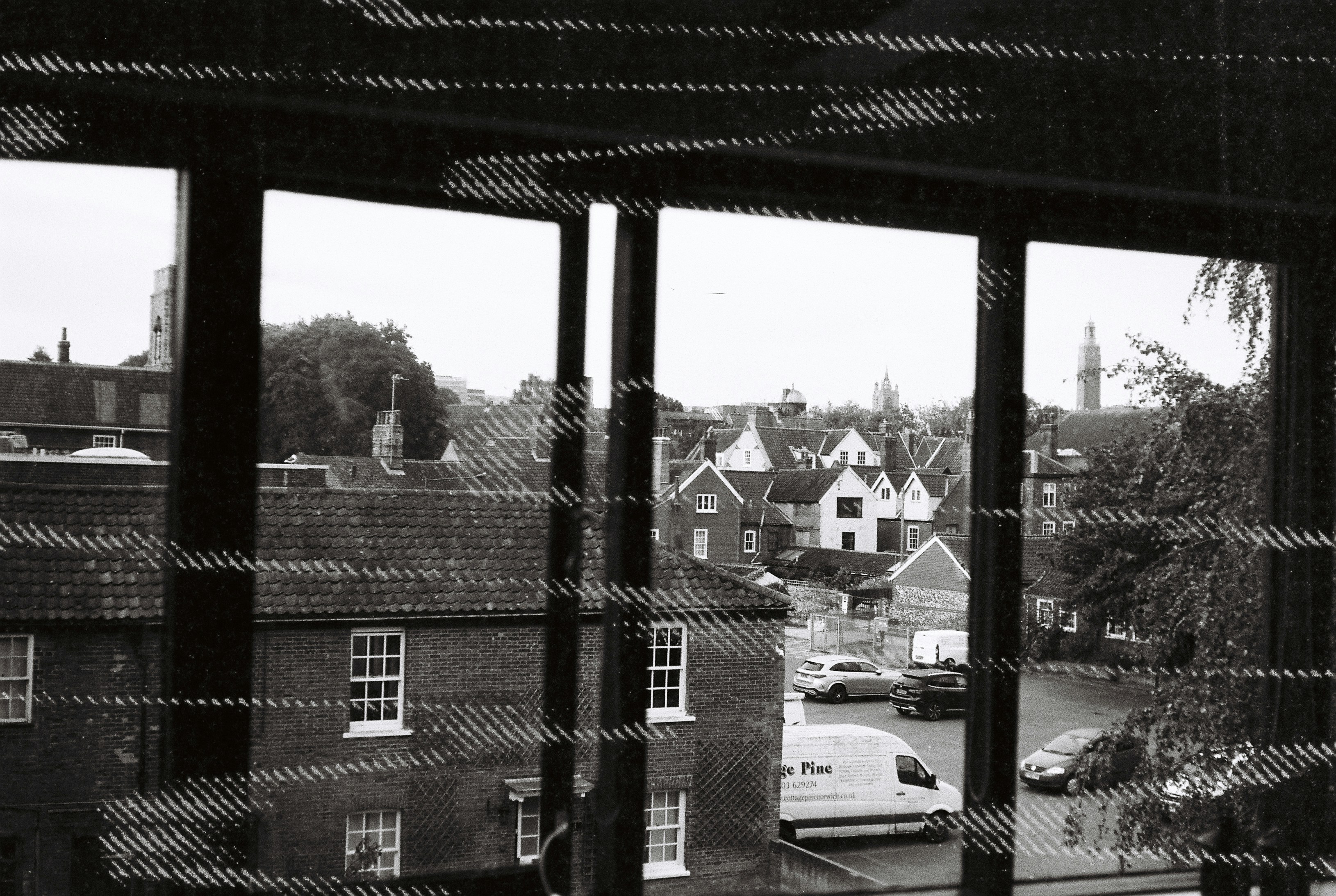 A view of brick buildings and a parking lot through a window with blinds
