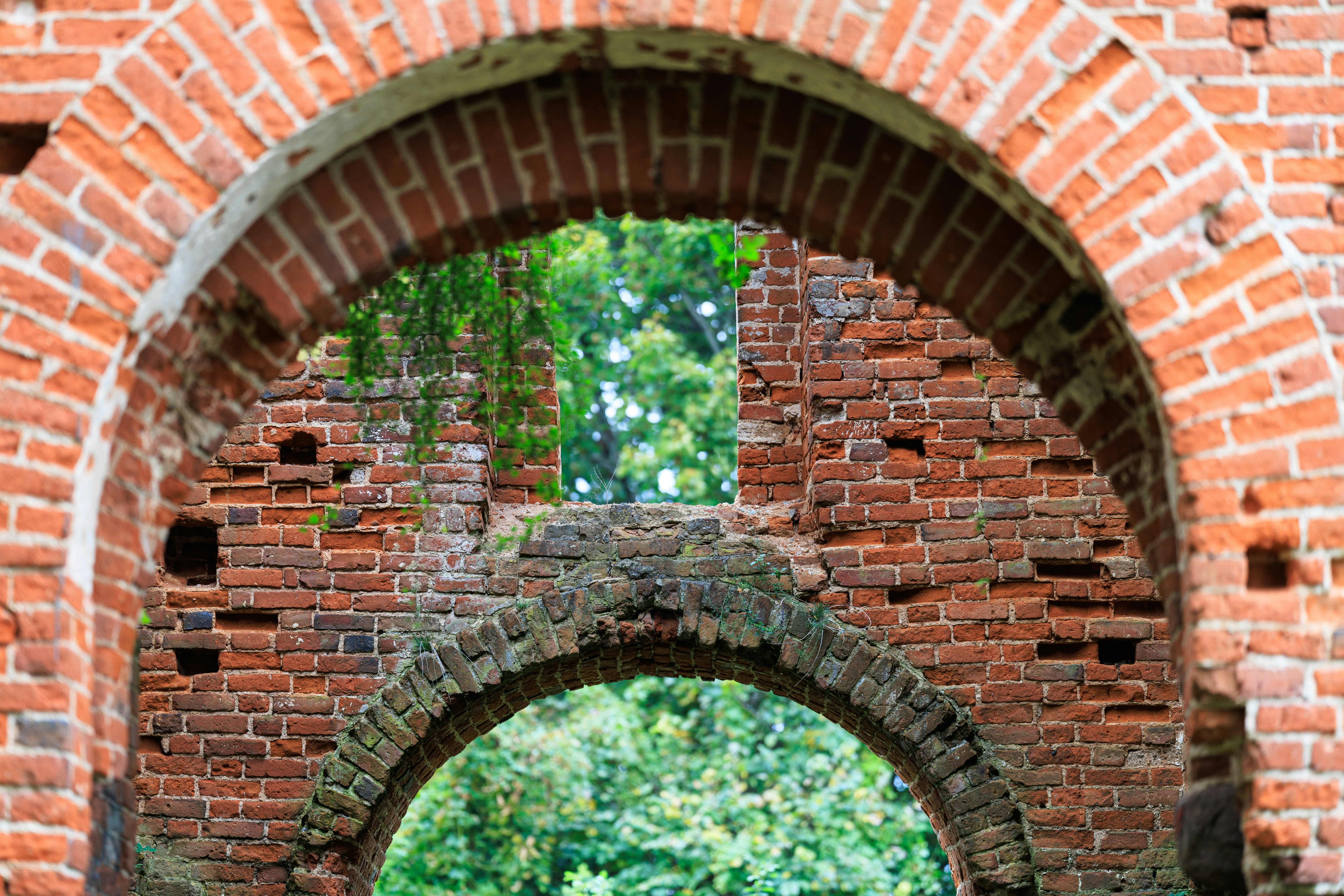 A weathered red brick archway framing a view of green trees