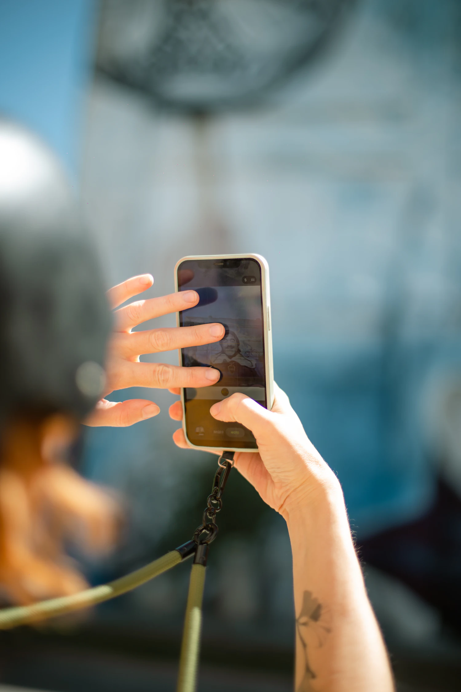 A phone hanging from a Loop Strap while its owner frames a photo
