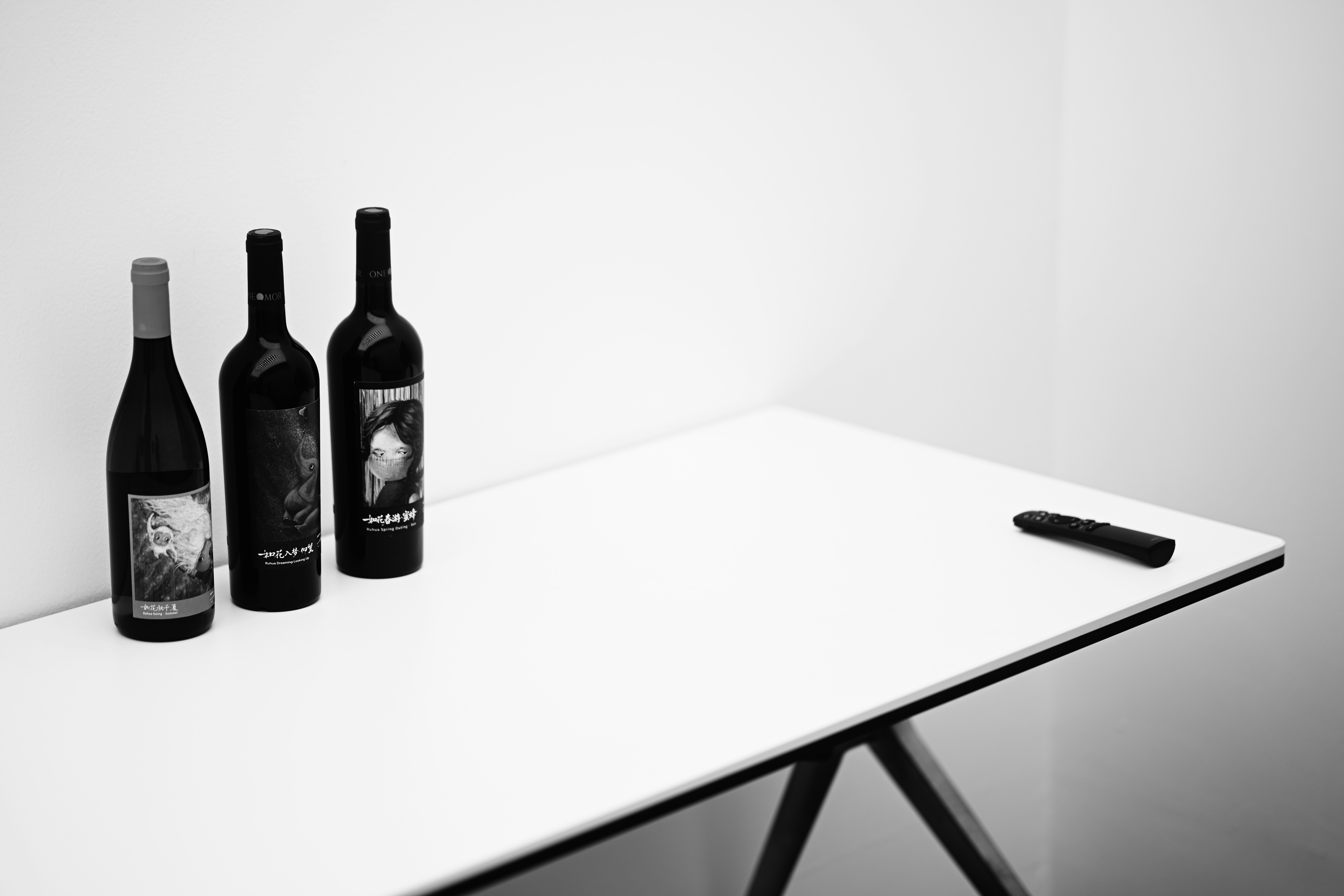 Three wine bottles and a remote control on a white table