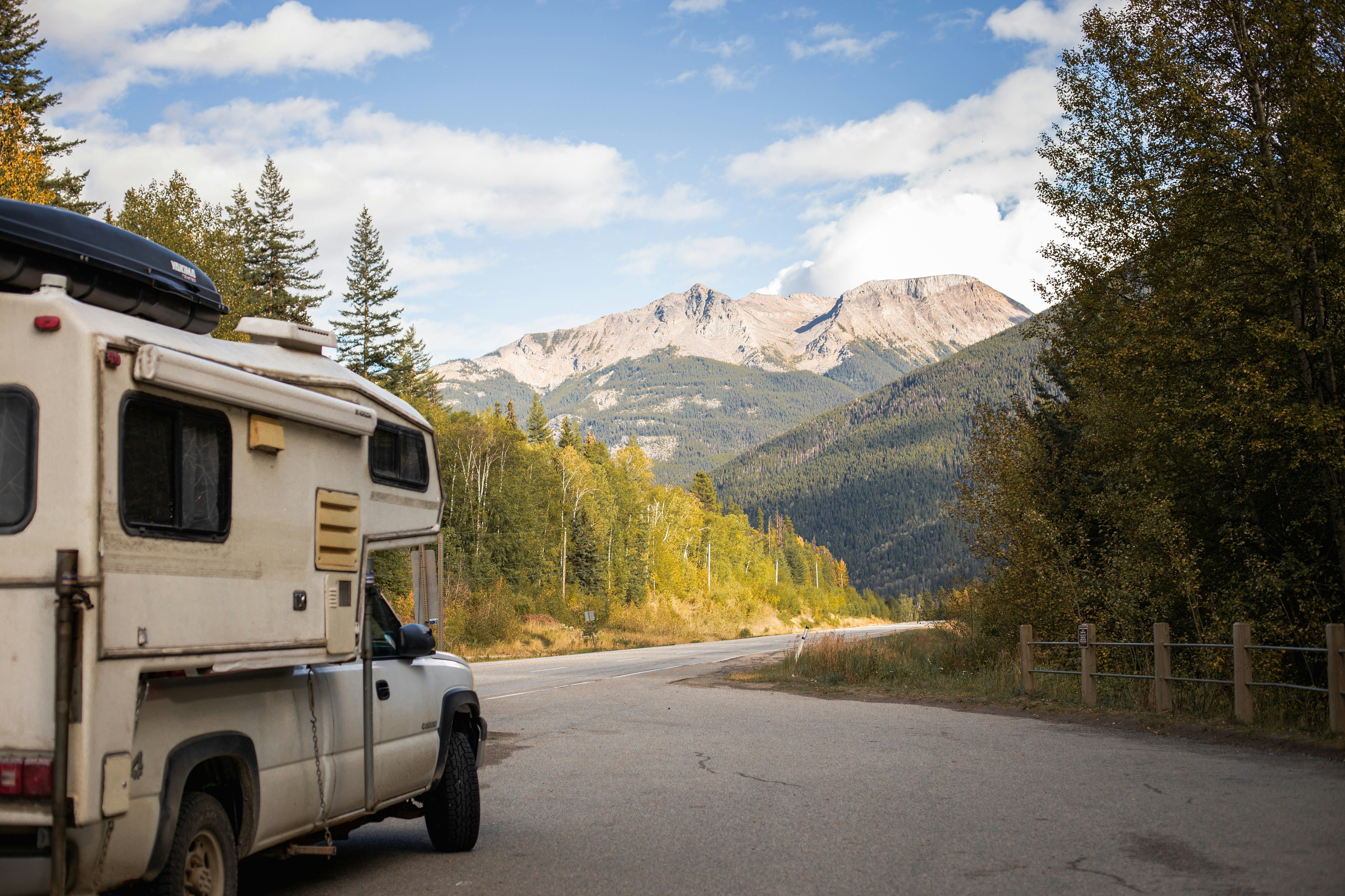 Camping-car cellule sur pick-up arrêté au bord d'une route de montagne bordée d'arbres aux couleurs d'automne
