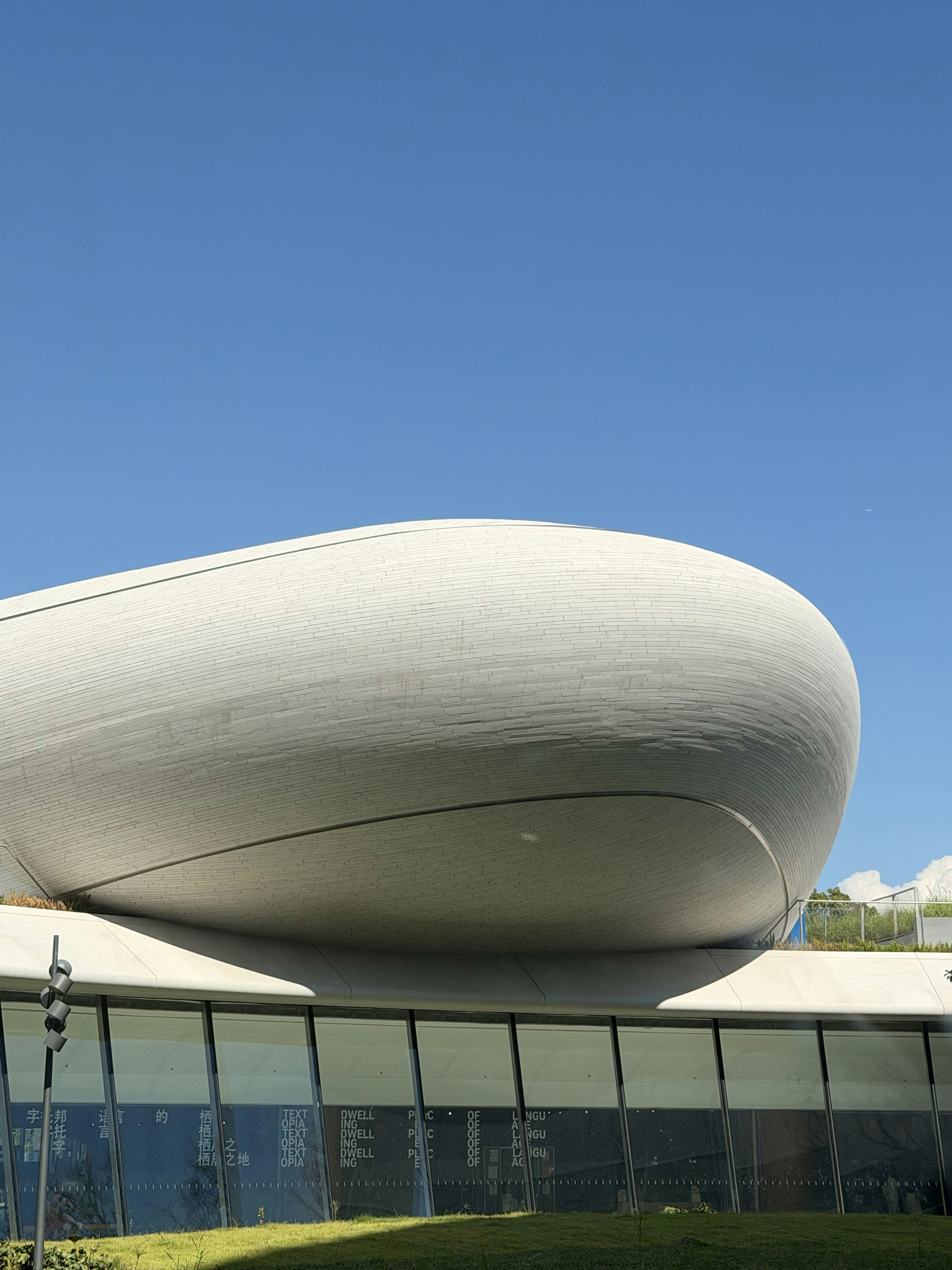 A curved white building with a tiled facade against a clear blue sky
