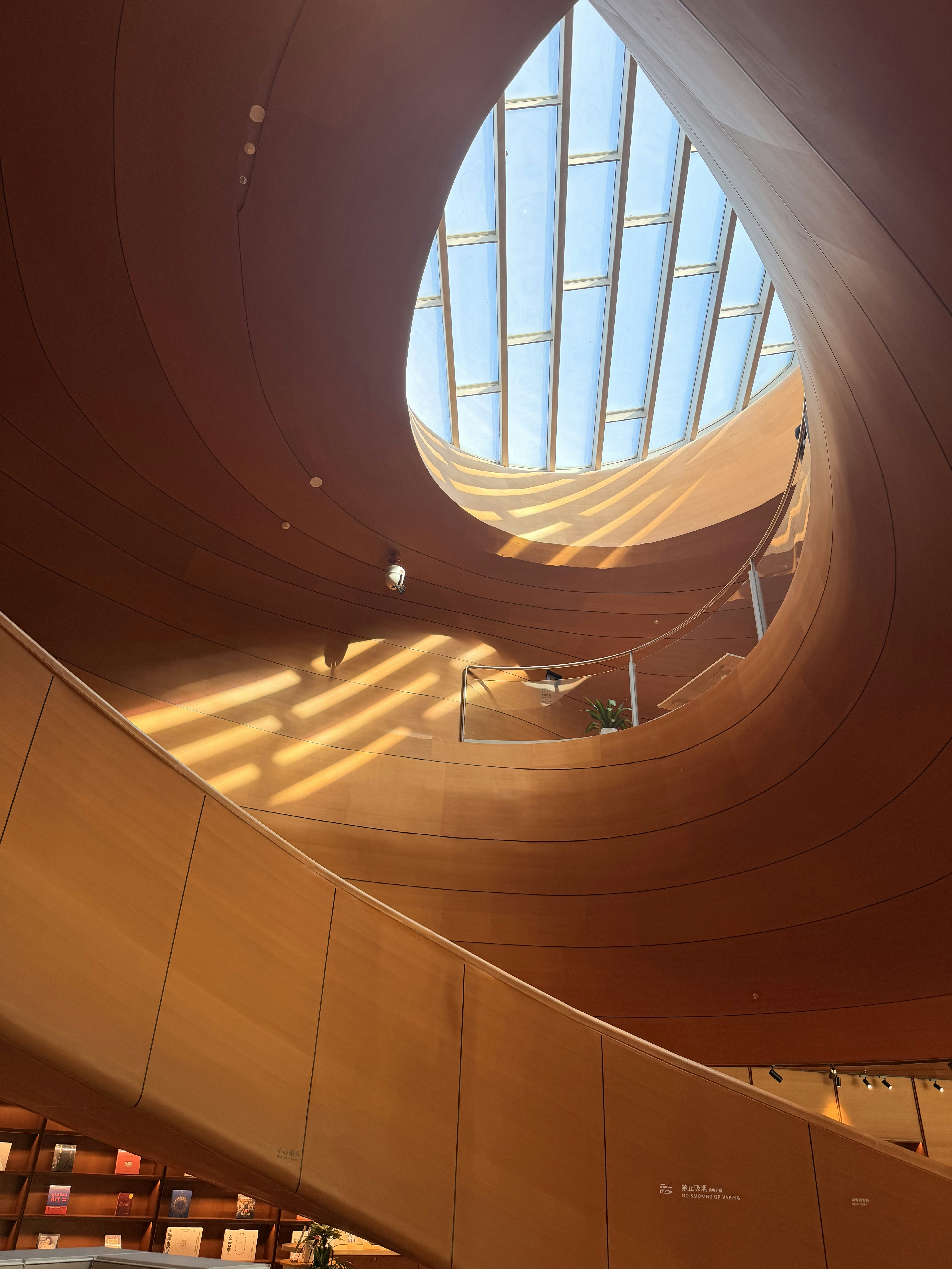 A curved wooden staircase spiraling beneath a large circular skylight with warm sunlight