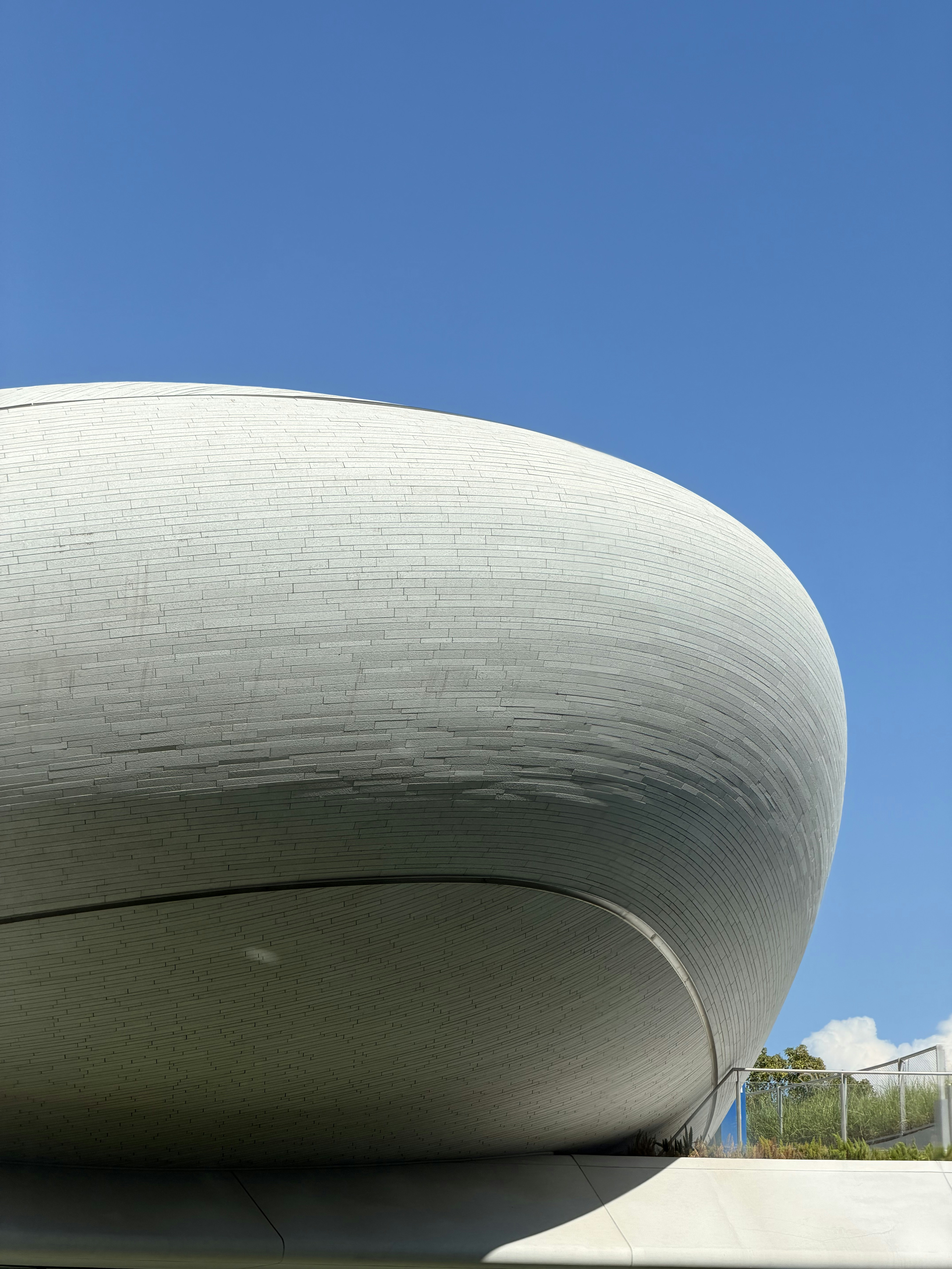 A curved white brick building exterior against a clear blue sky