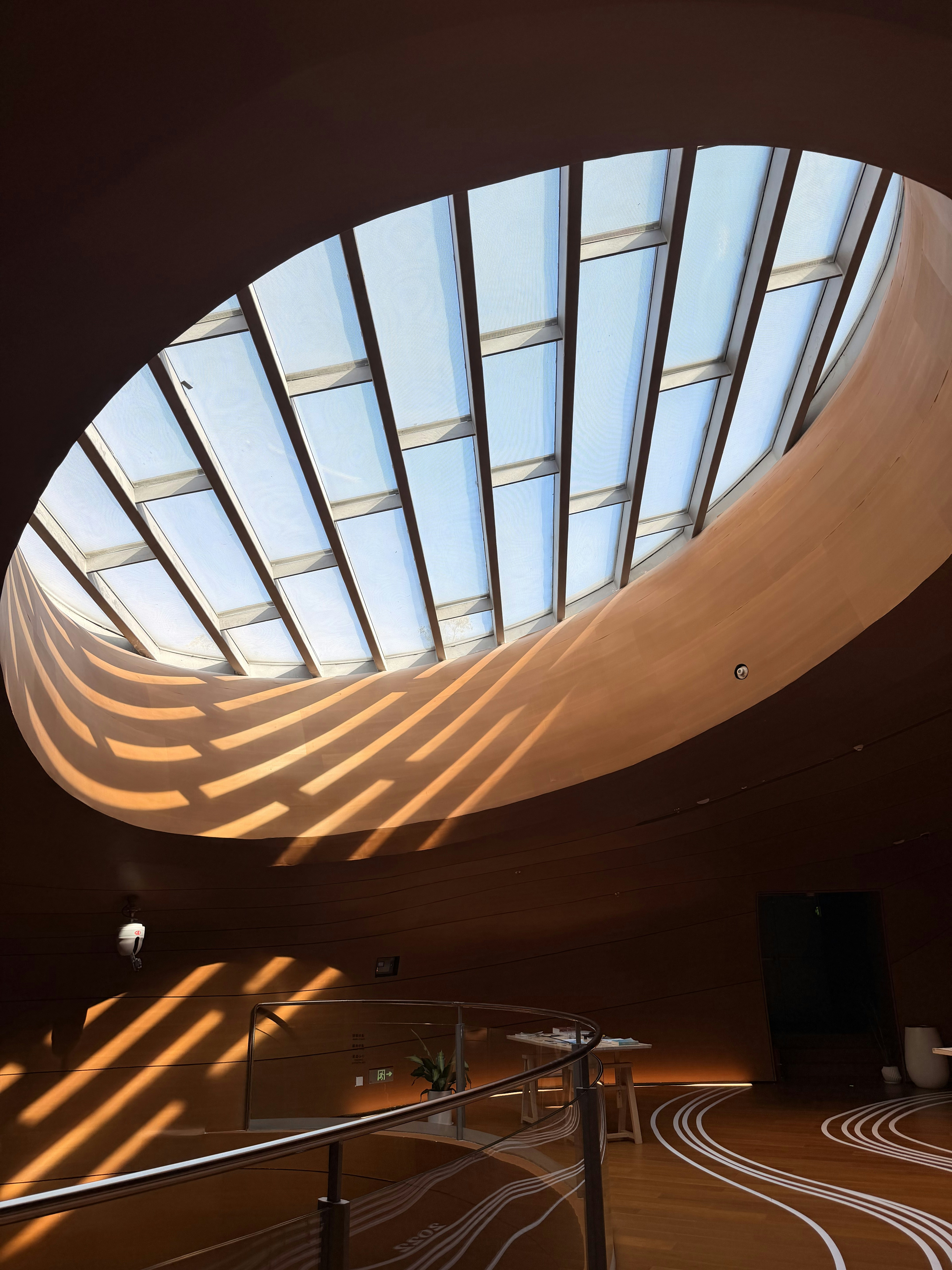 A circular skylight casting long shadows across curved wooden walls in a modern interior