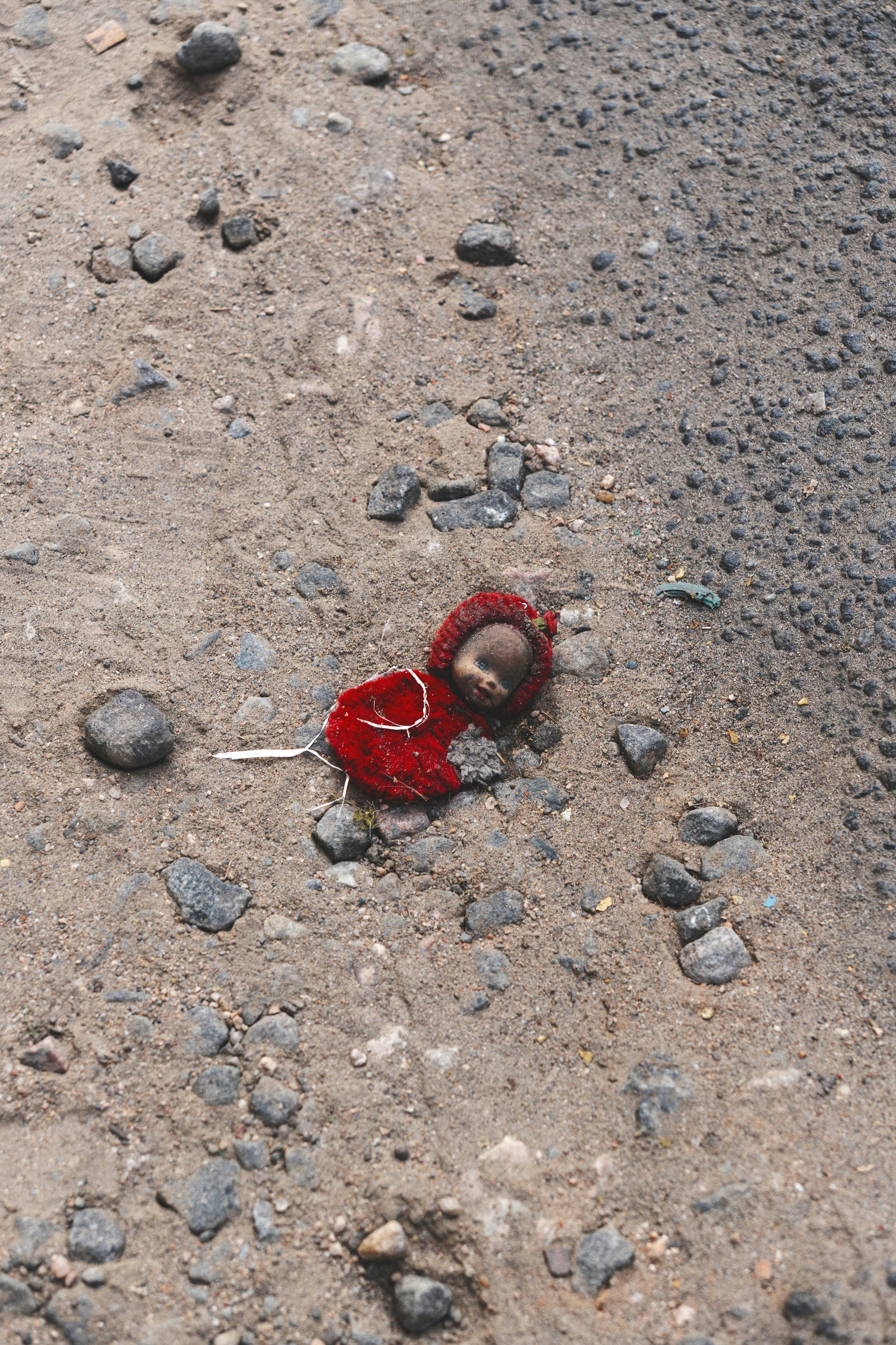 A small doll in a red fuzzy outfit lying on sandy ground