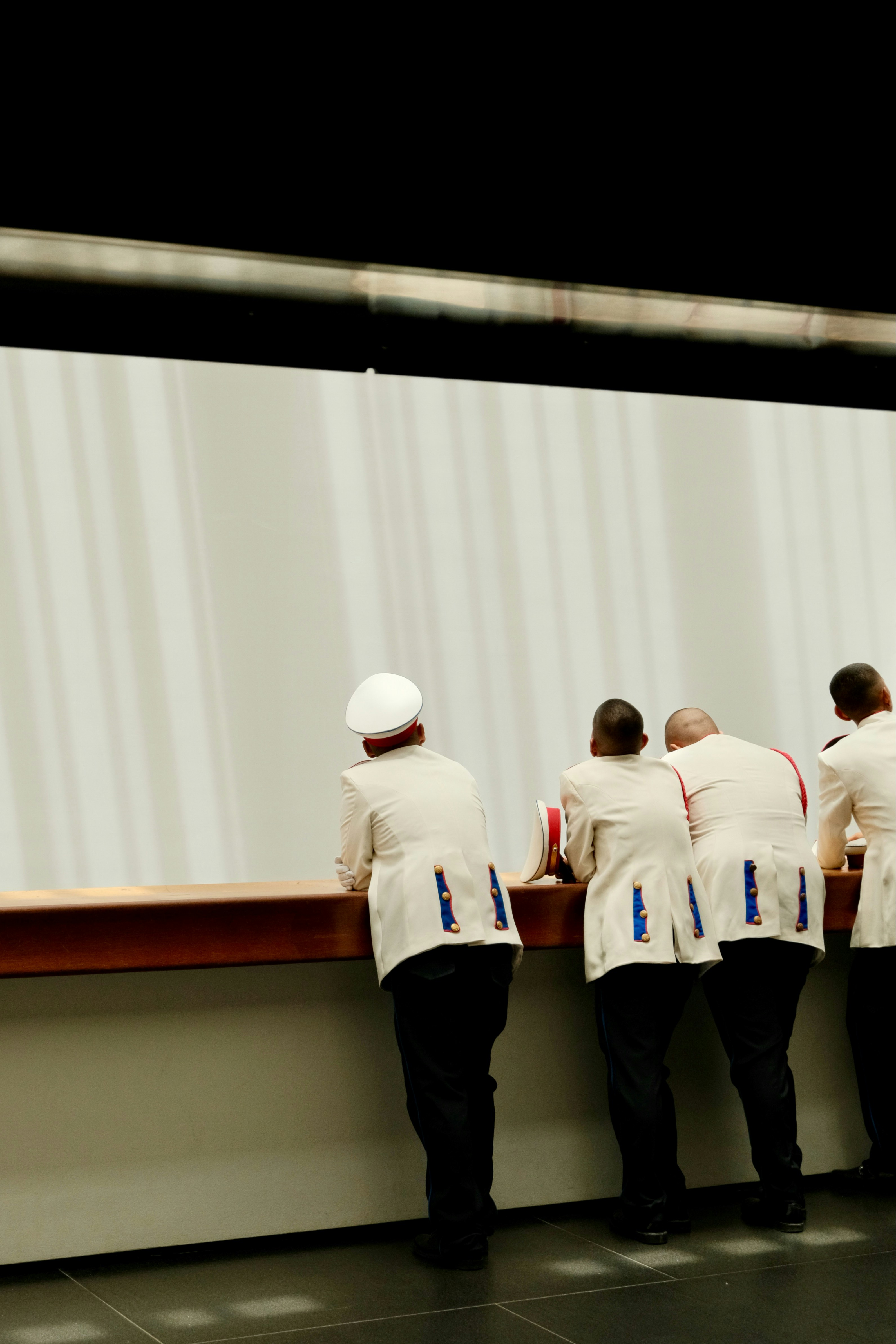Four people in white military dress uniforms leaning against a wooden railing