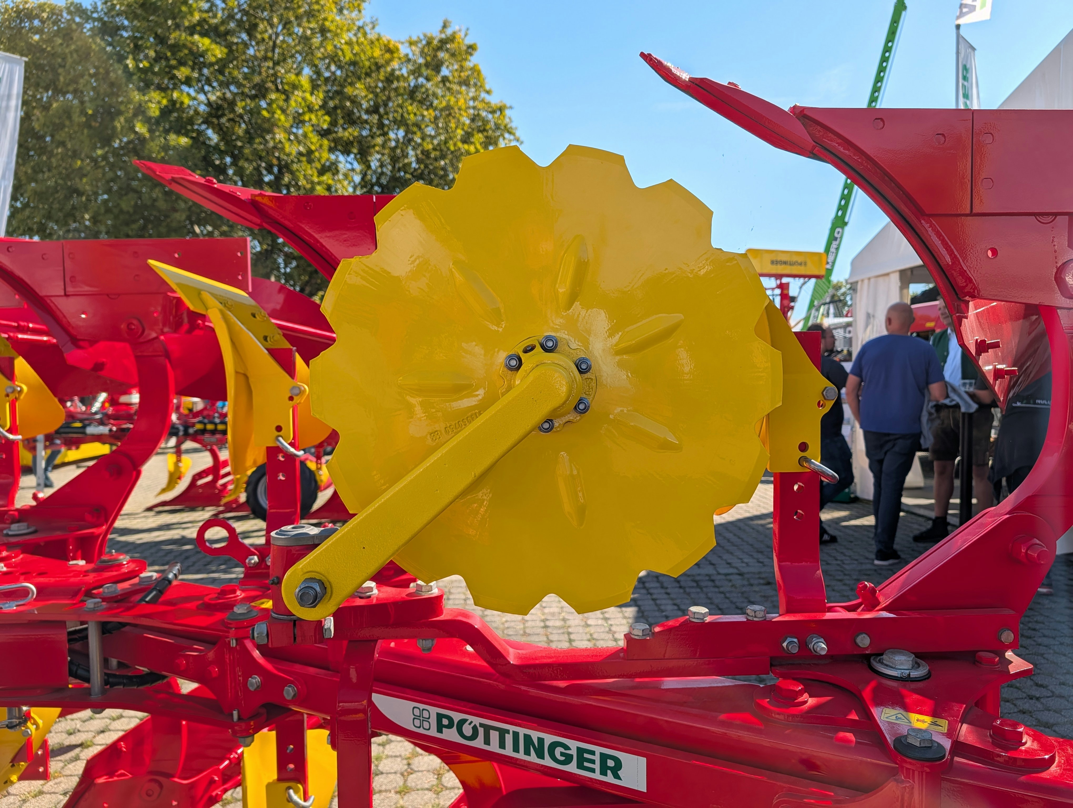 A yellow notched disc on a red agricultural plow in a sunny outdoor lot