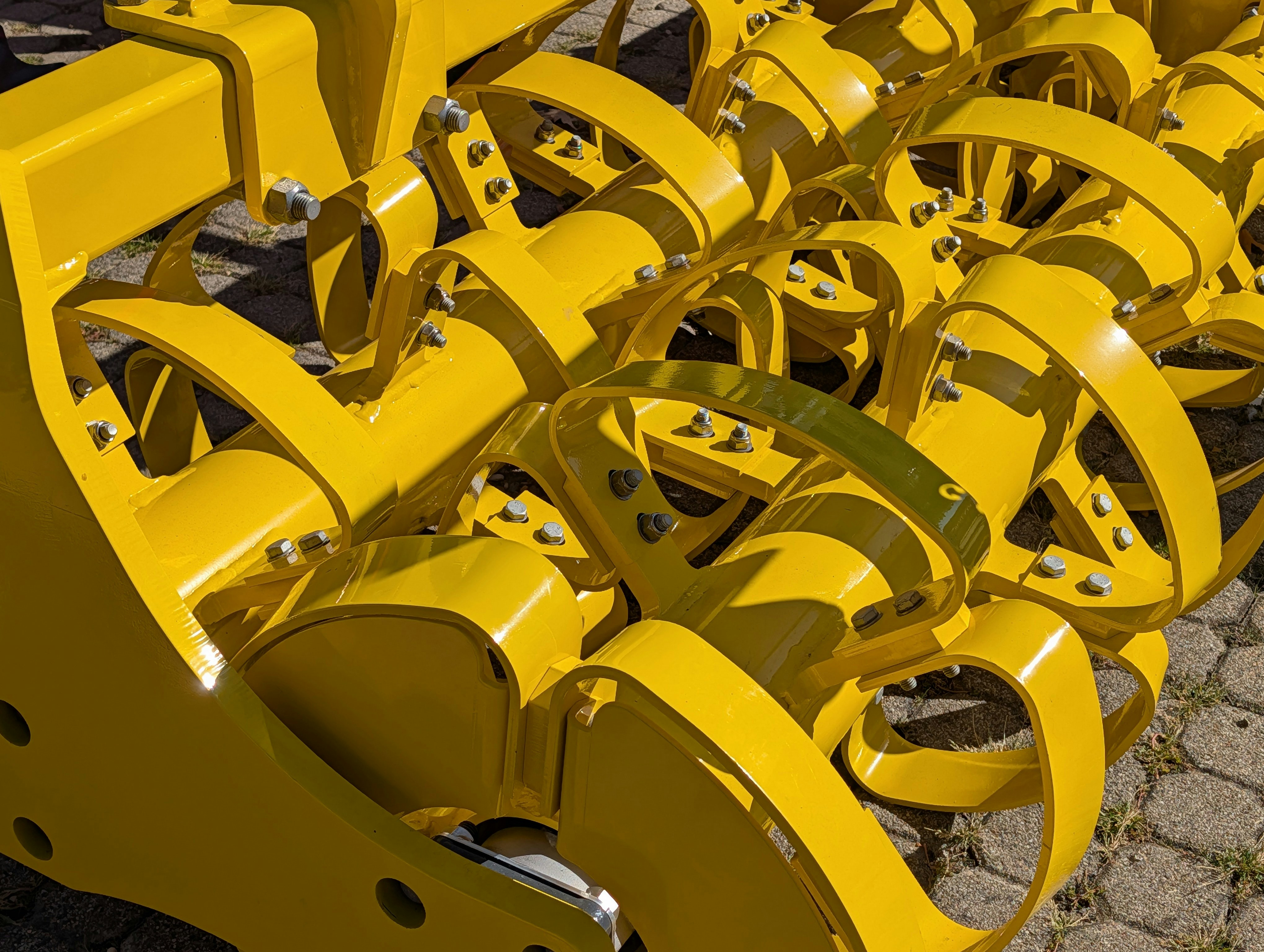 A bright yellow agricultural soil roller with curved metal blades on a paved surface