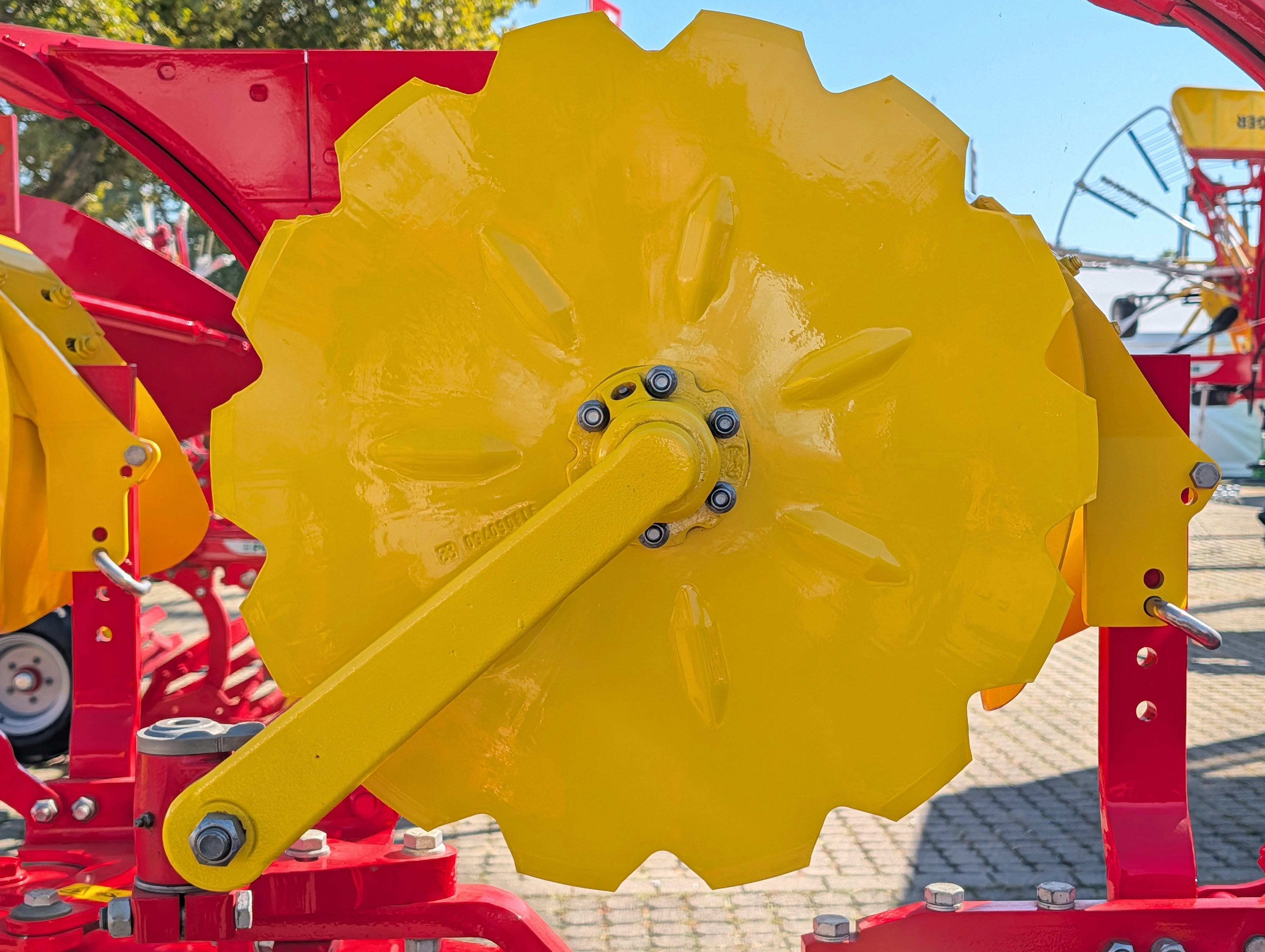 A bright yellow notched disc blade on a red agricultural machine