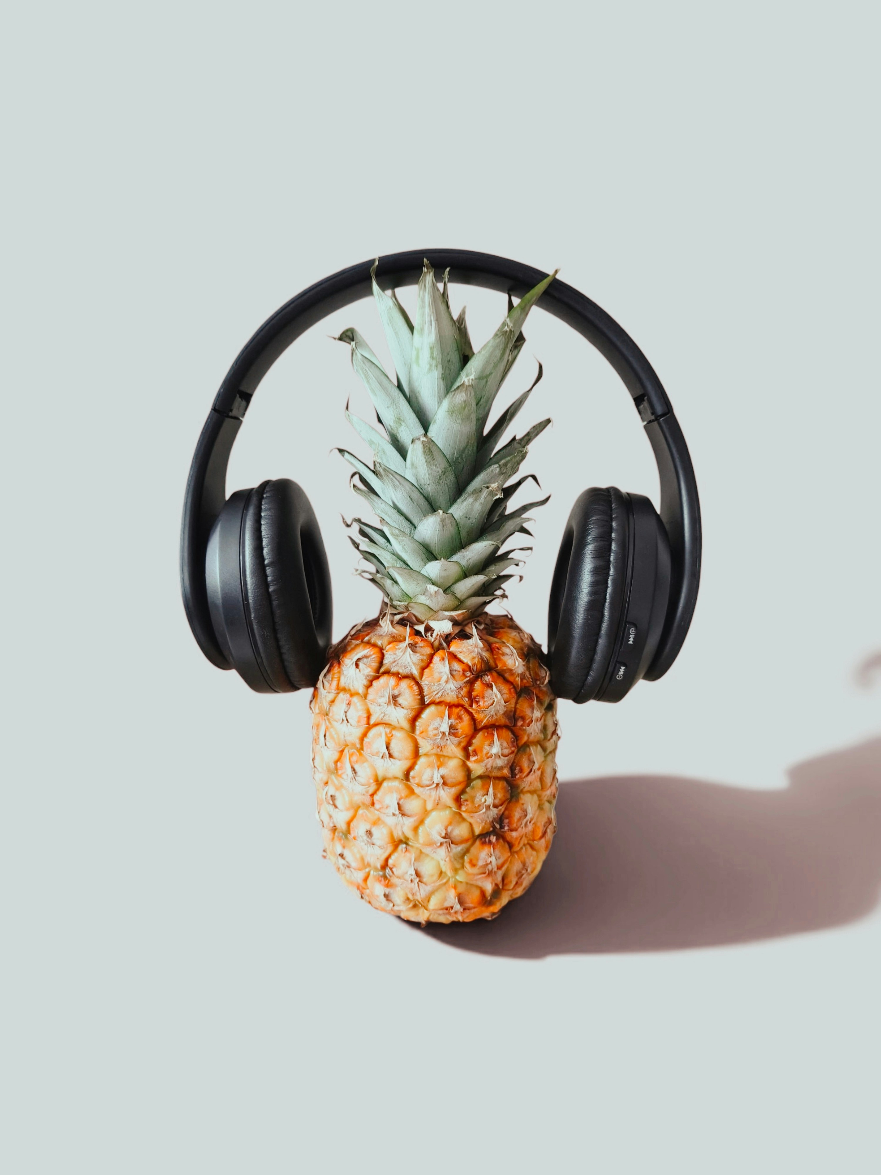 A fresh pineapple wearing black over-ear headphones against a light grey background
