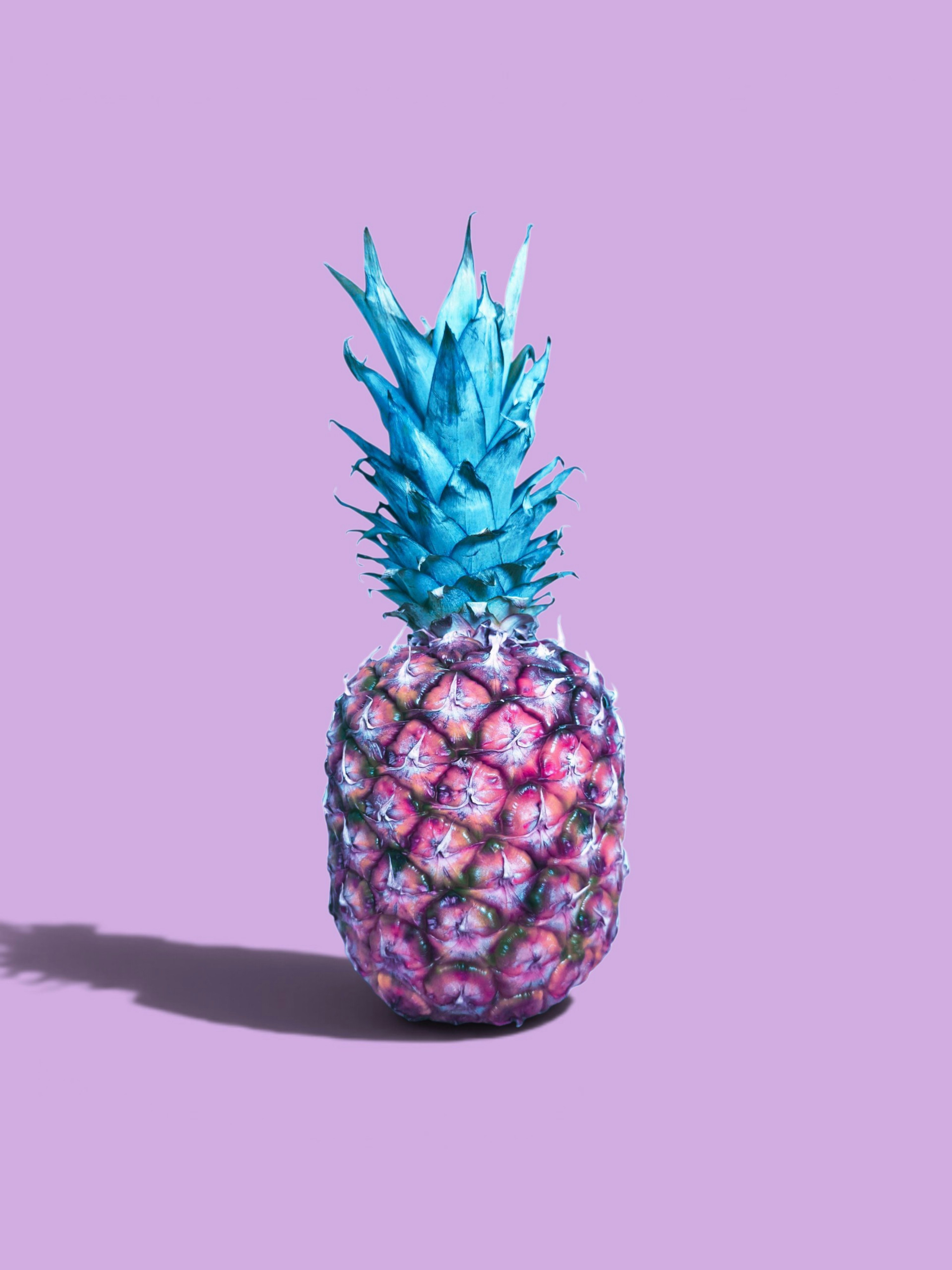 A pineapple with blue leaves and a pink and purple body on a light purple background