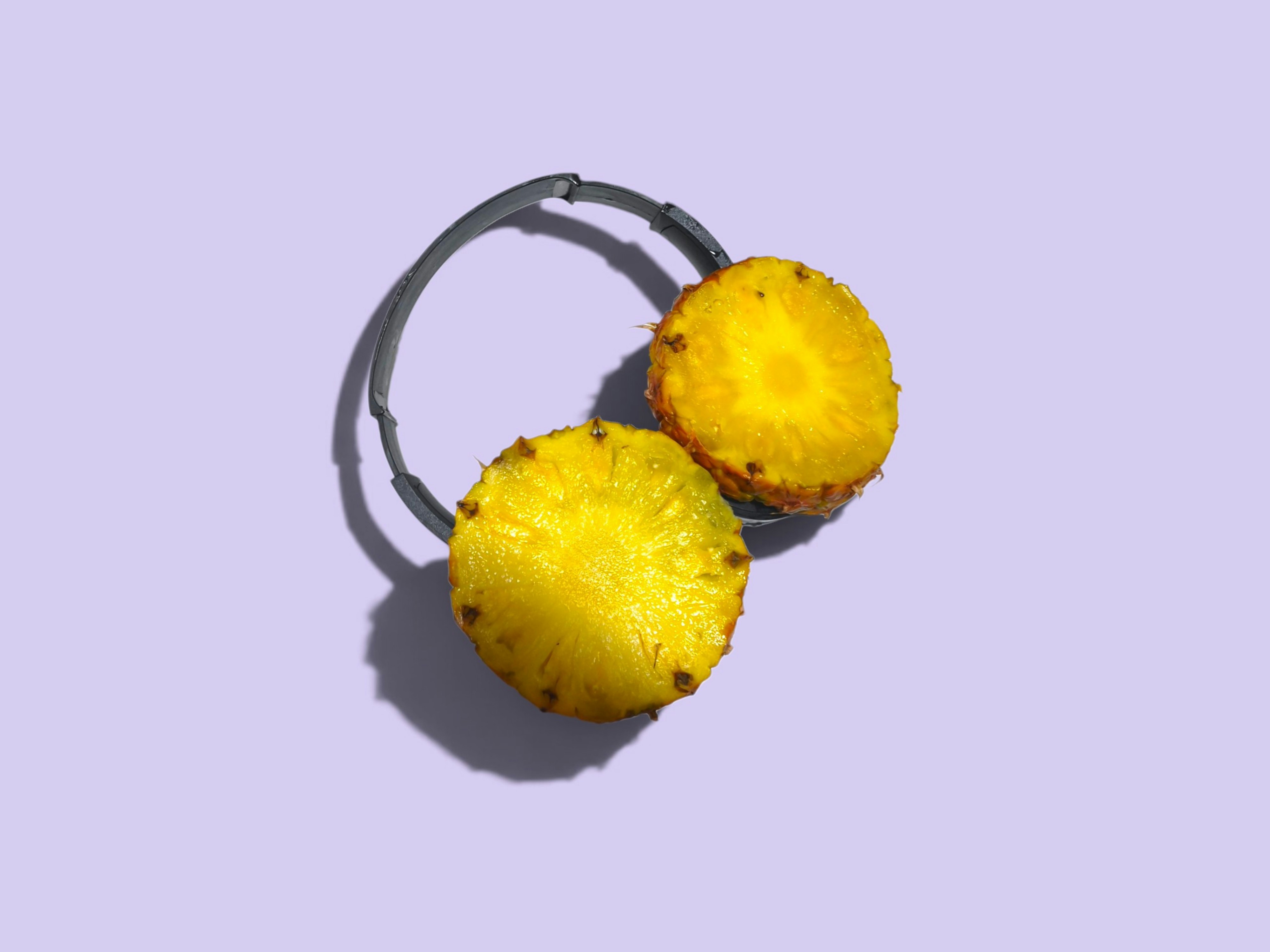 Two pineapple slices attached to a black headband on a light purple background