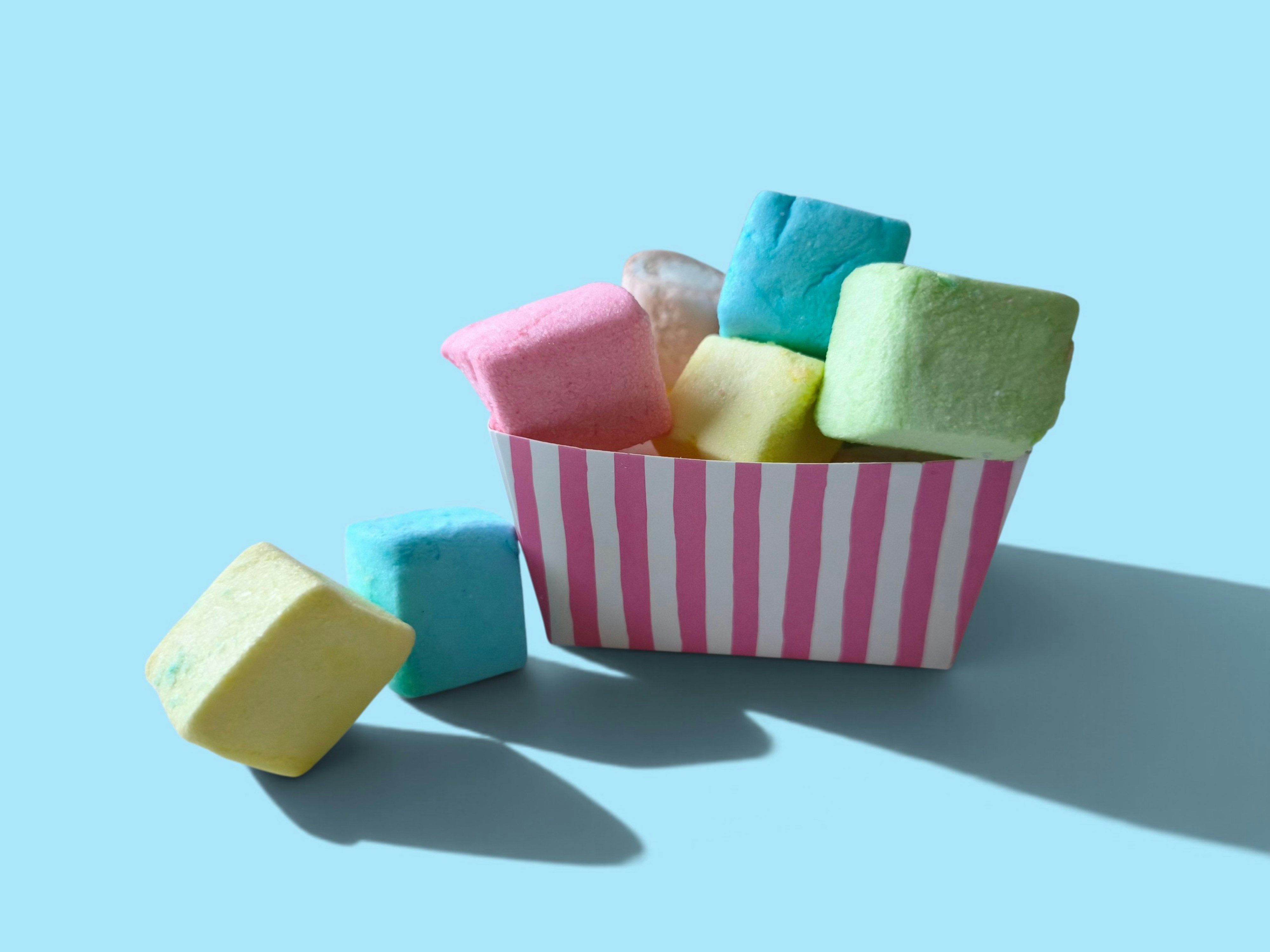 Pastel colored marshmallows in a striped paper container on a light blue surface