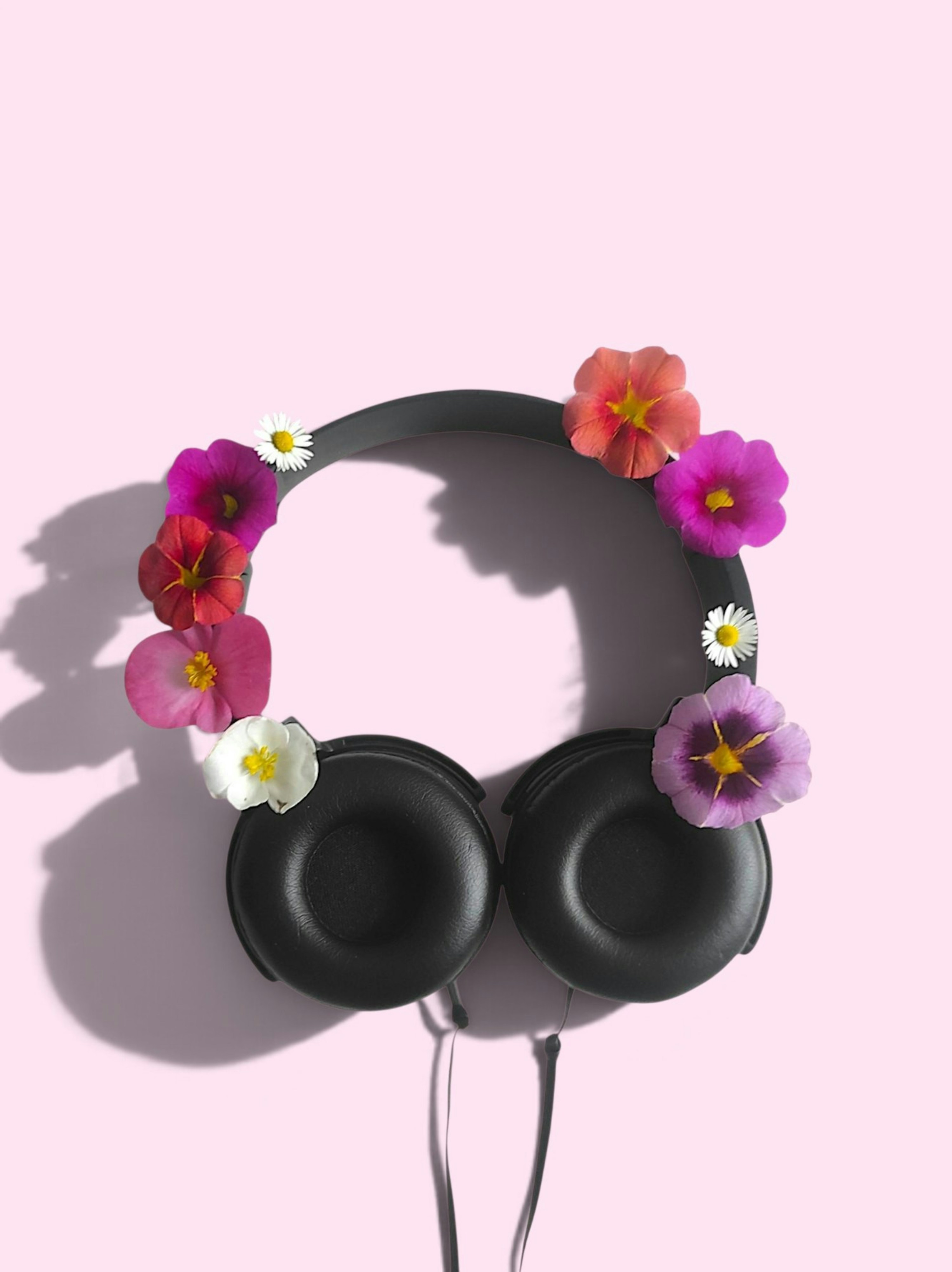 Black headphones decorated with colorful flowers on a light pink background