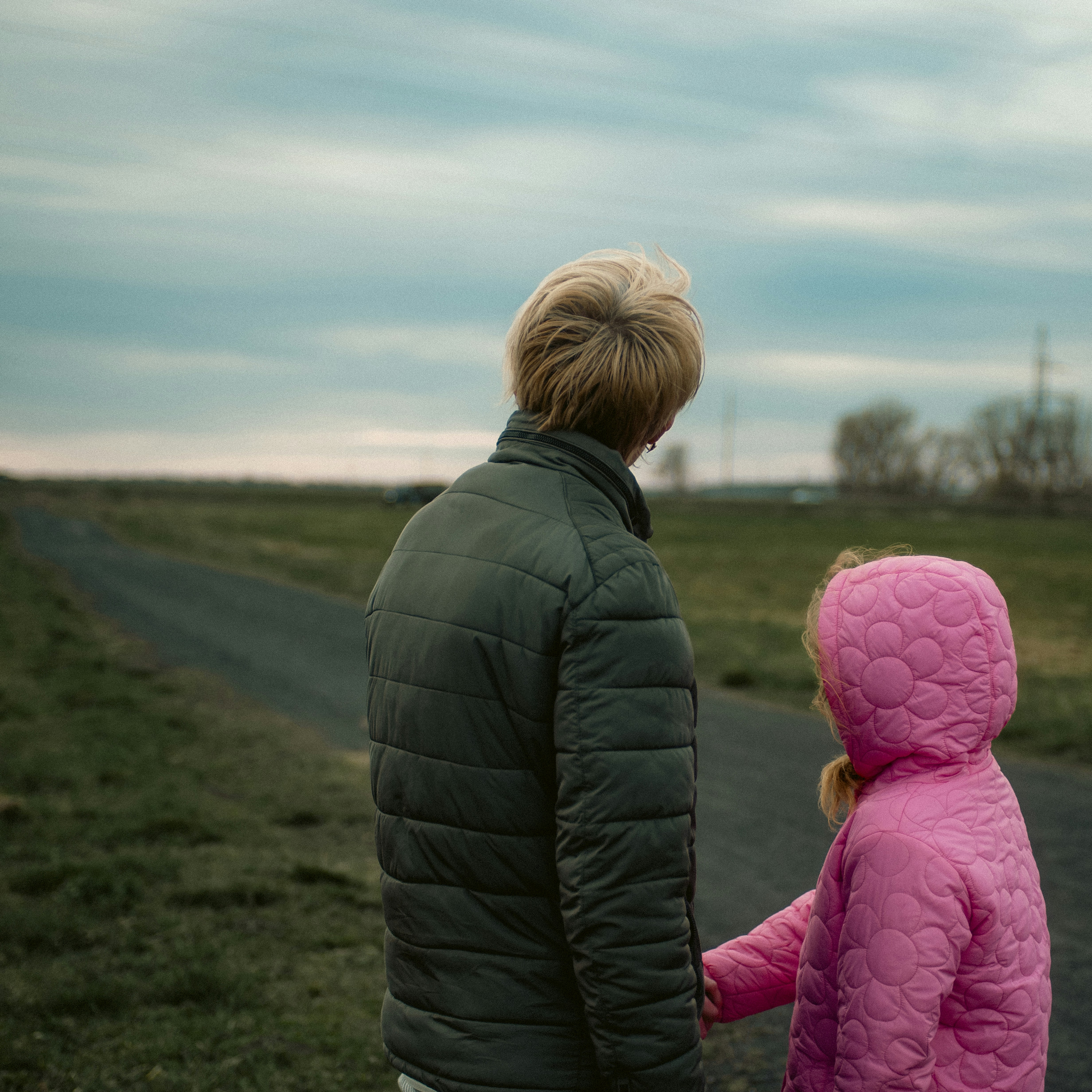 grandchild: An adult and a child in a pink hooded jacket walking along a rural path