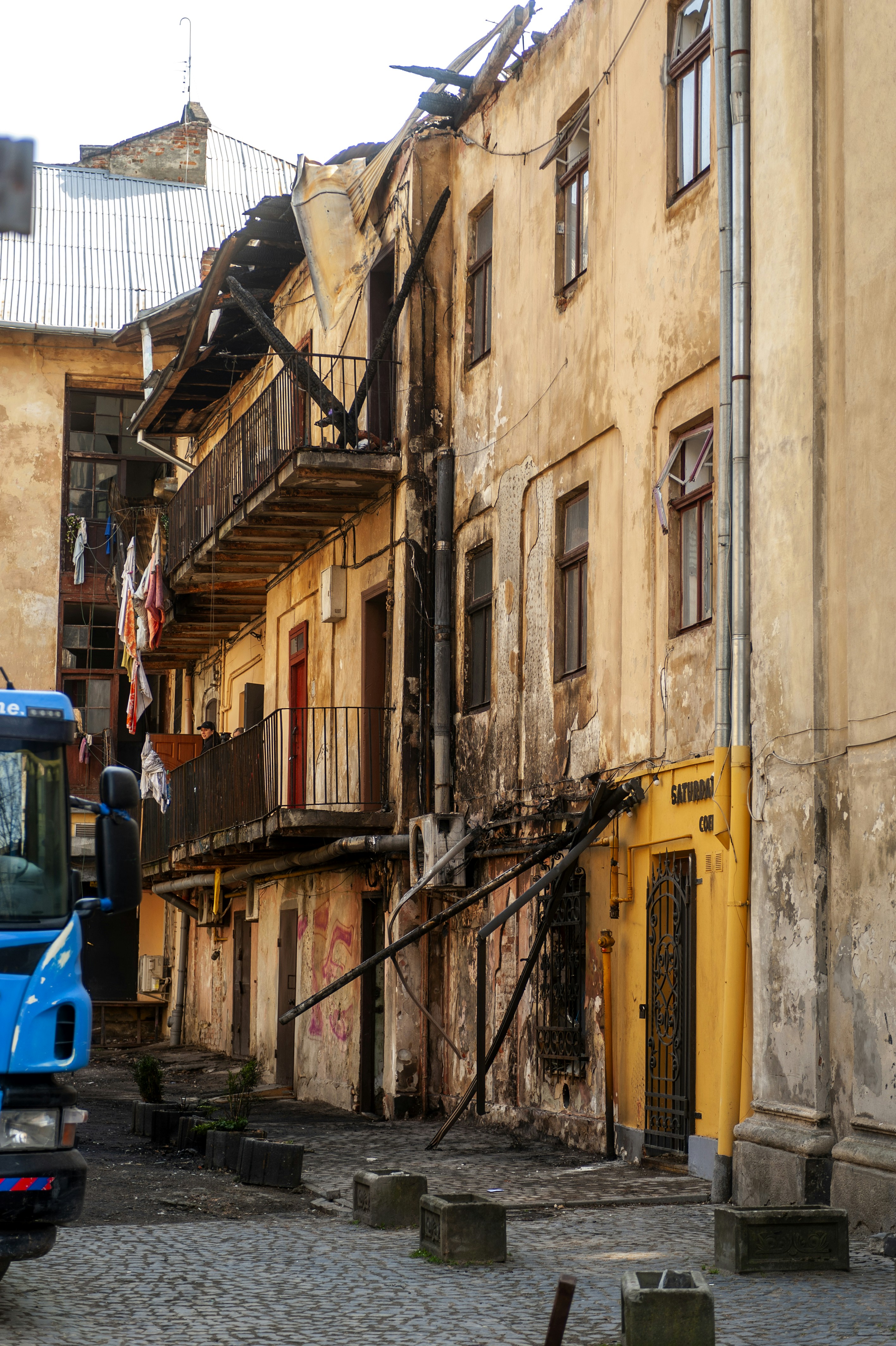 A damaged building with charred balconies and peeling yellow paint above a cobblestone street