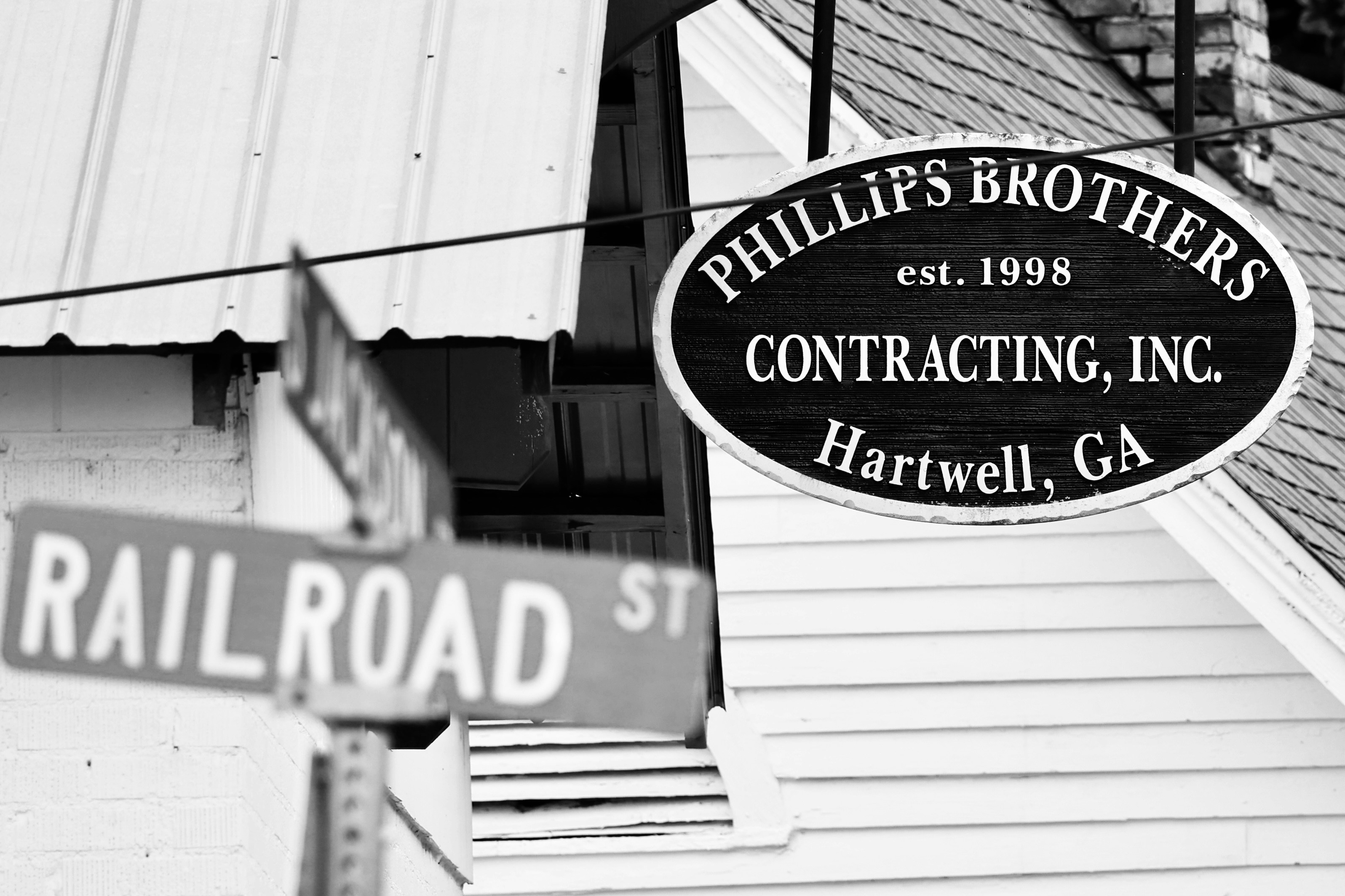 An oval business sign hanging outside a building beside a street sign