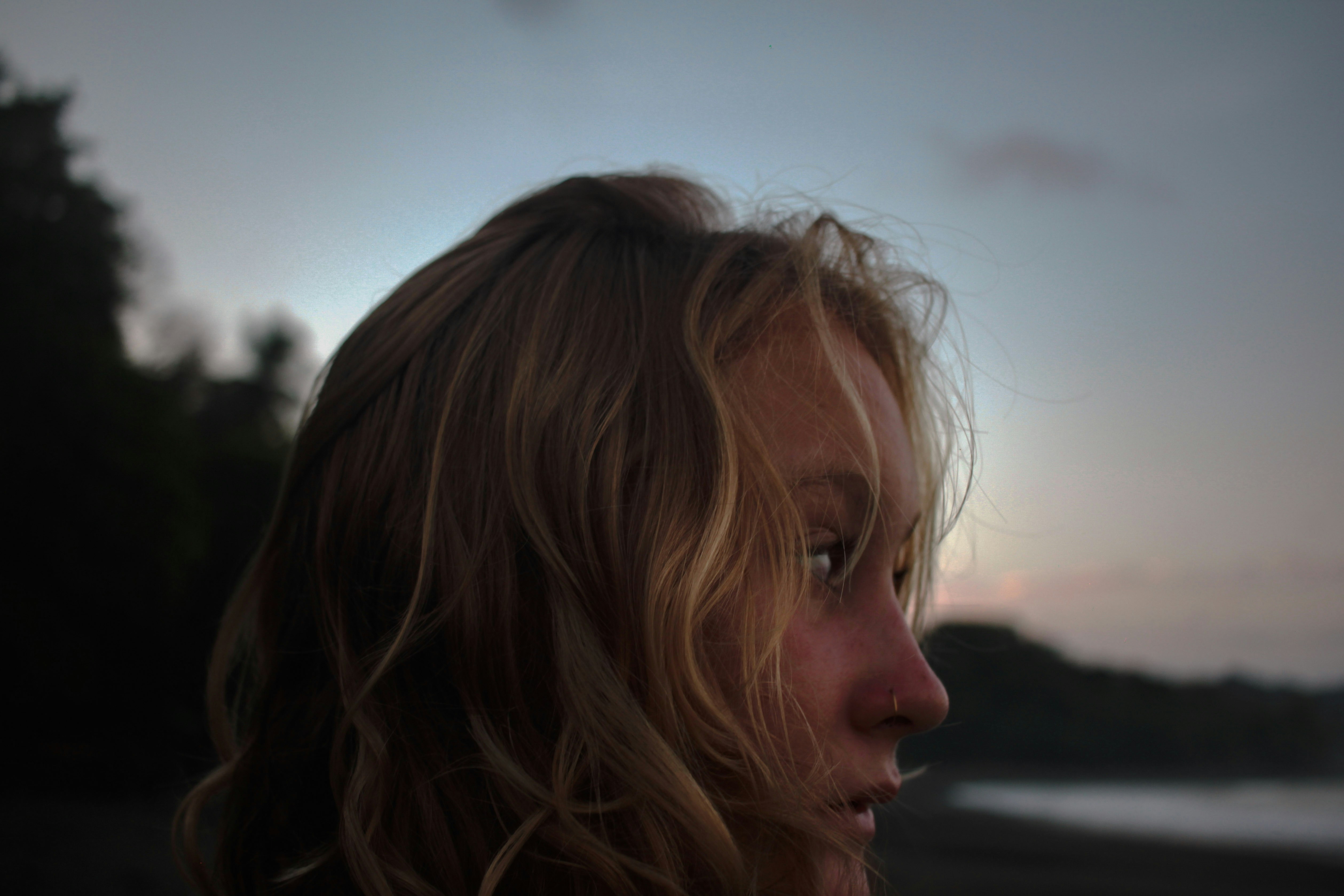 Profile of a woman with wavy blonde hair against a soft evening sky