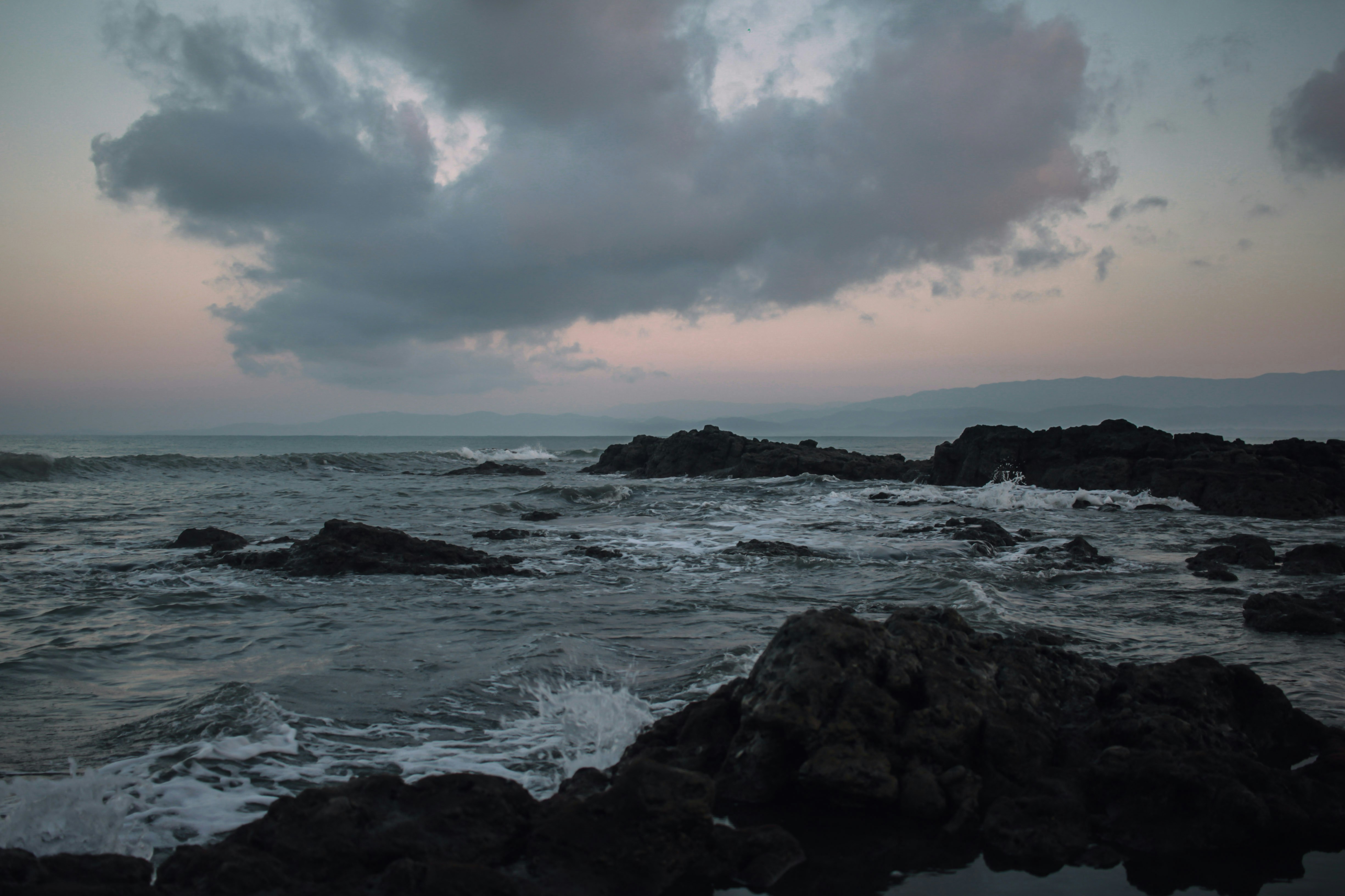 Dark rocky coastline with crashing waves under a cloudy sky at low light