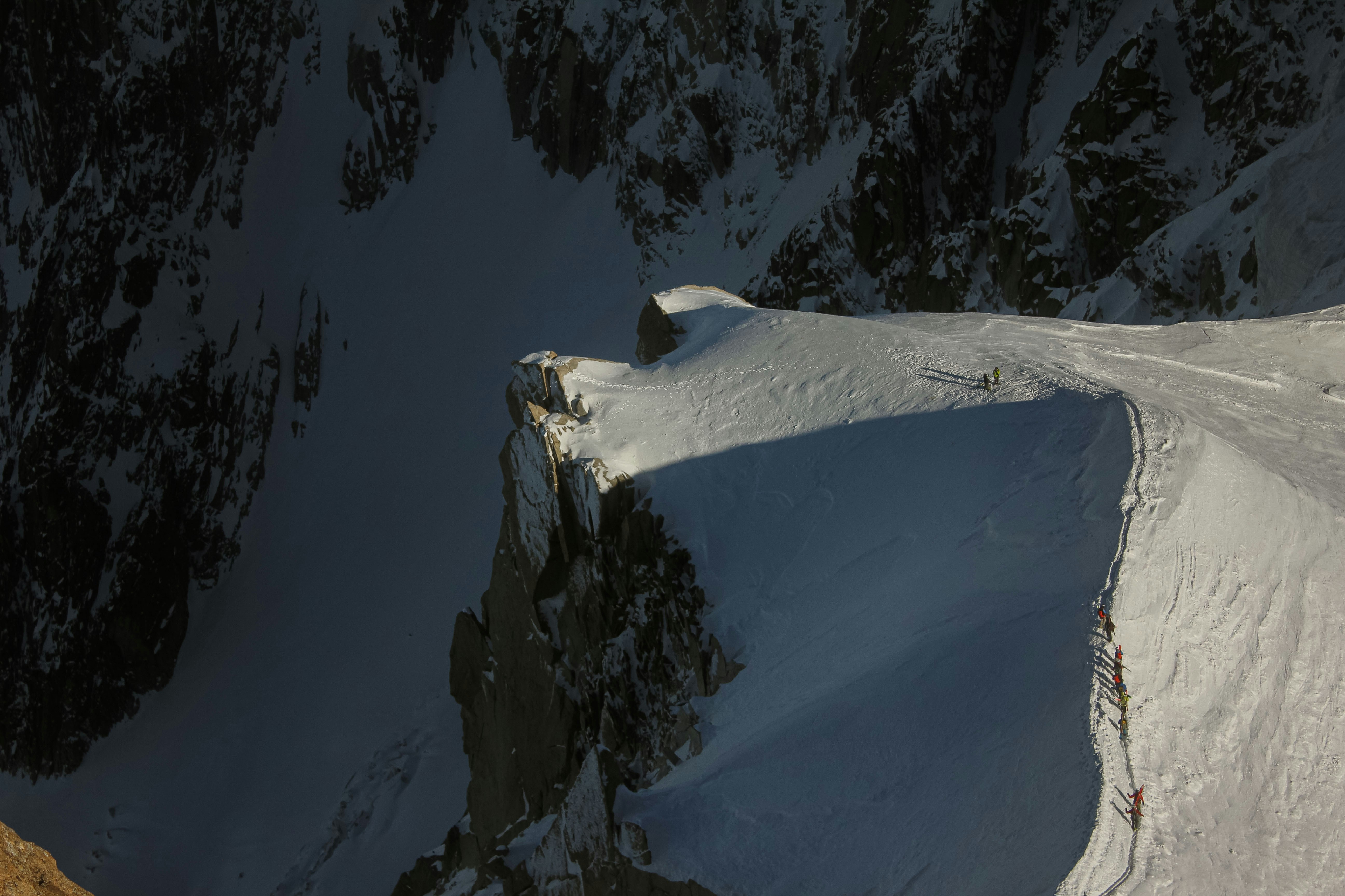 A line of mountaineers climbing a narrow snow ridge on a steep mountain face