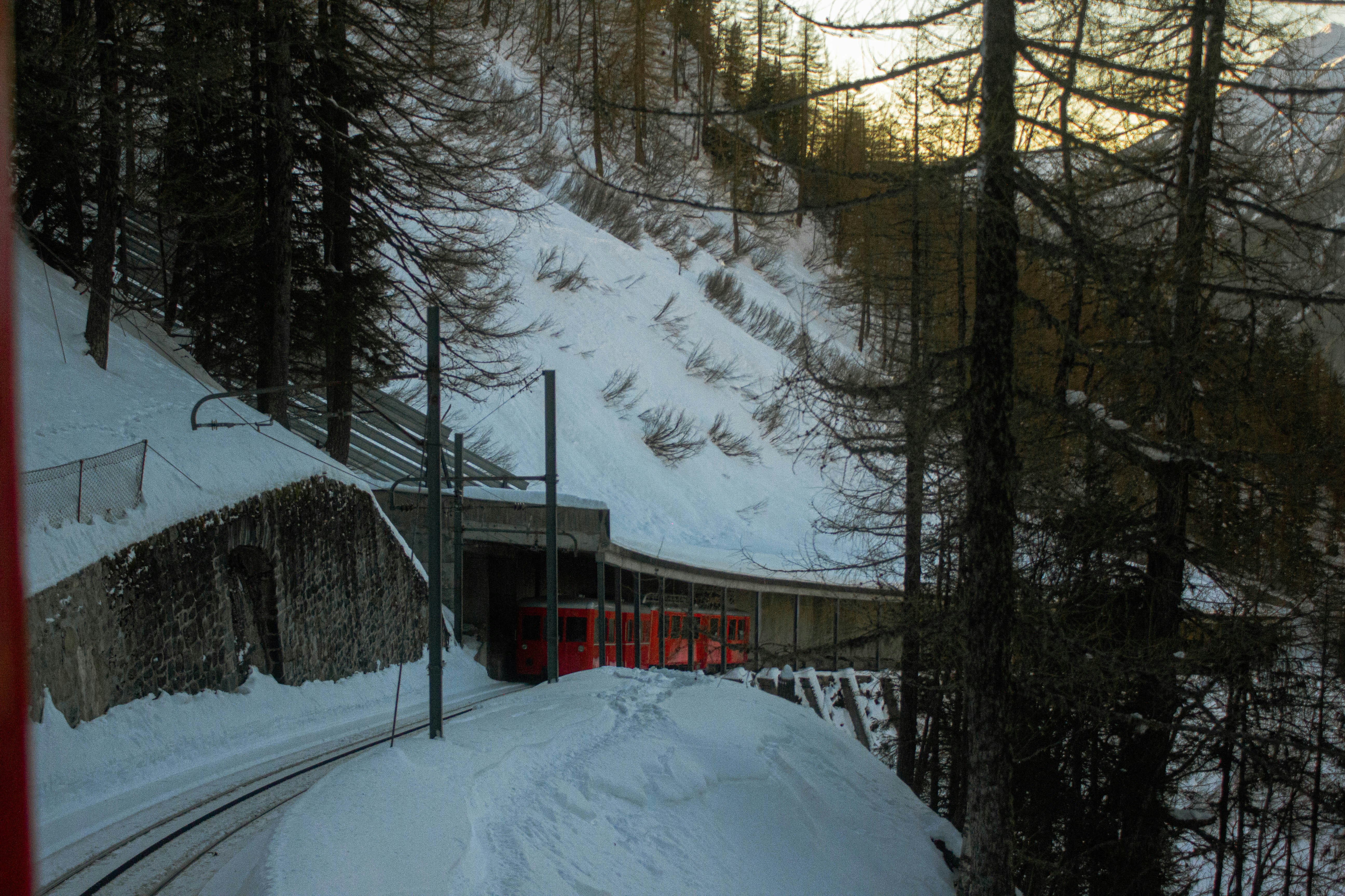 A red train emerging from a tunnel into a snowy mountain forest