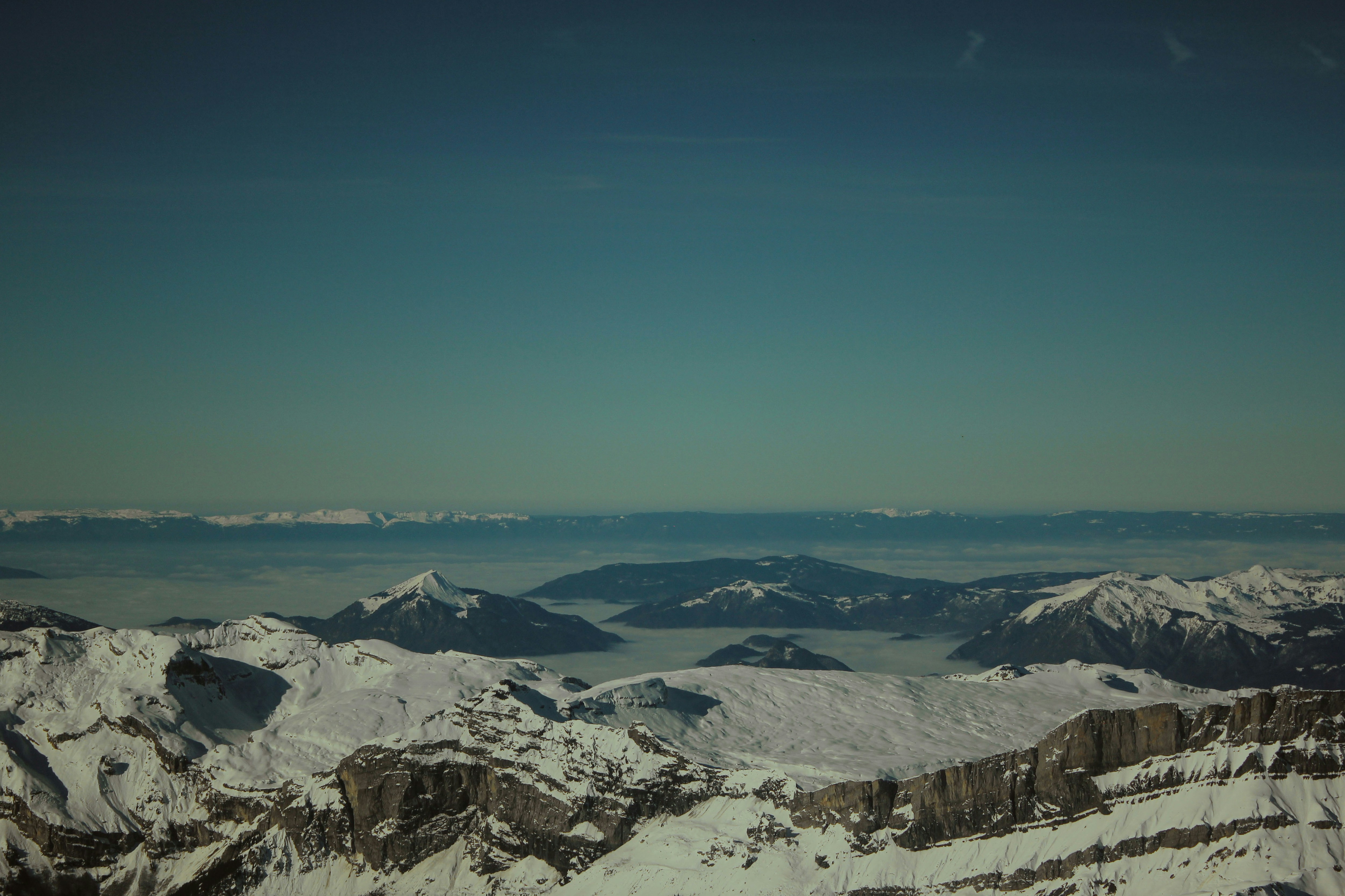Snowy mountain peaks rising above a thick layer of valley fog under a clear sky