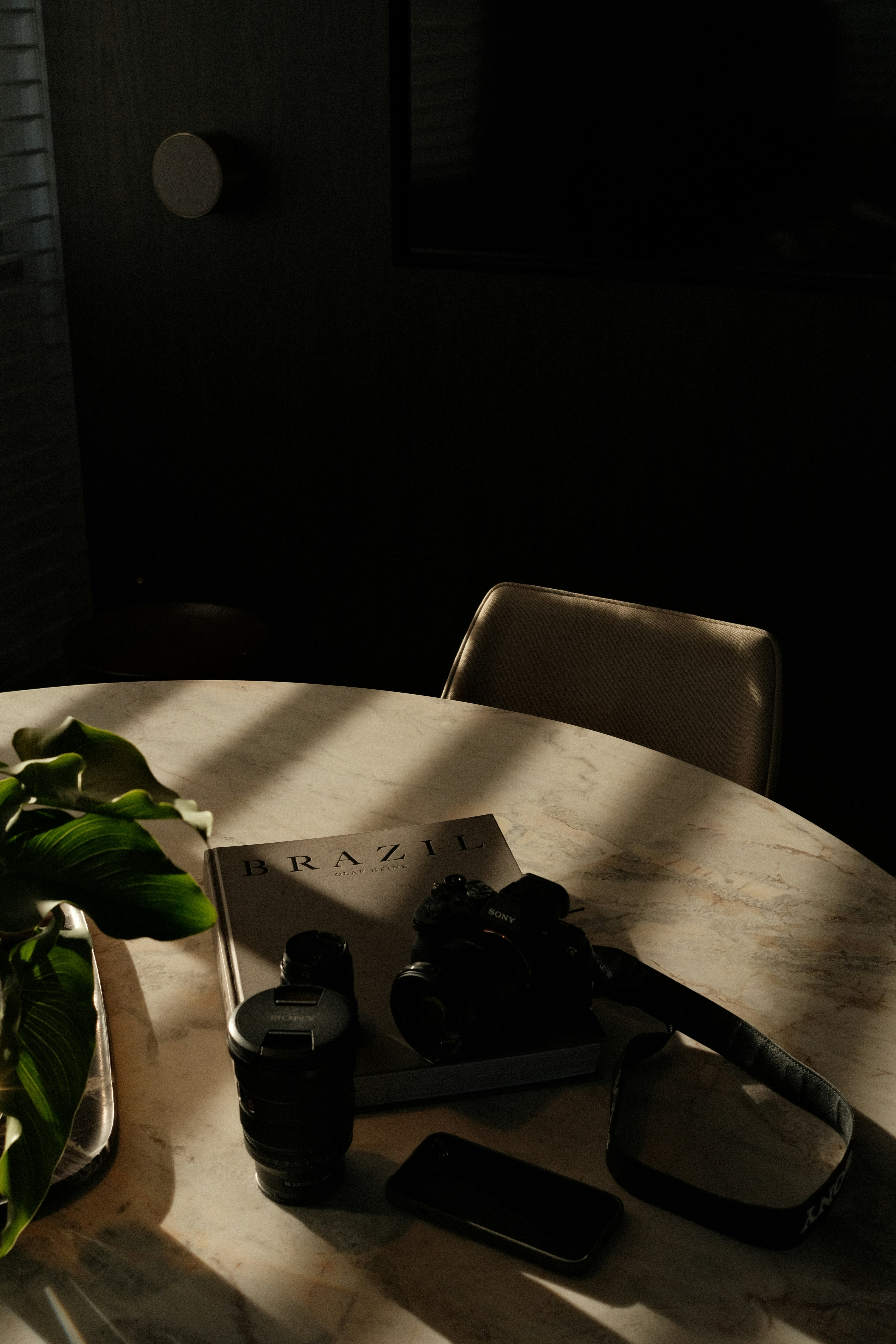 A camera, lenses, and a book on a marble table in sunlit room