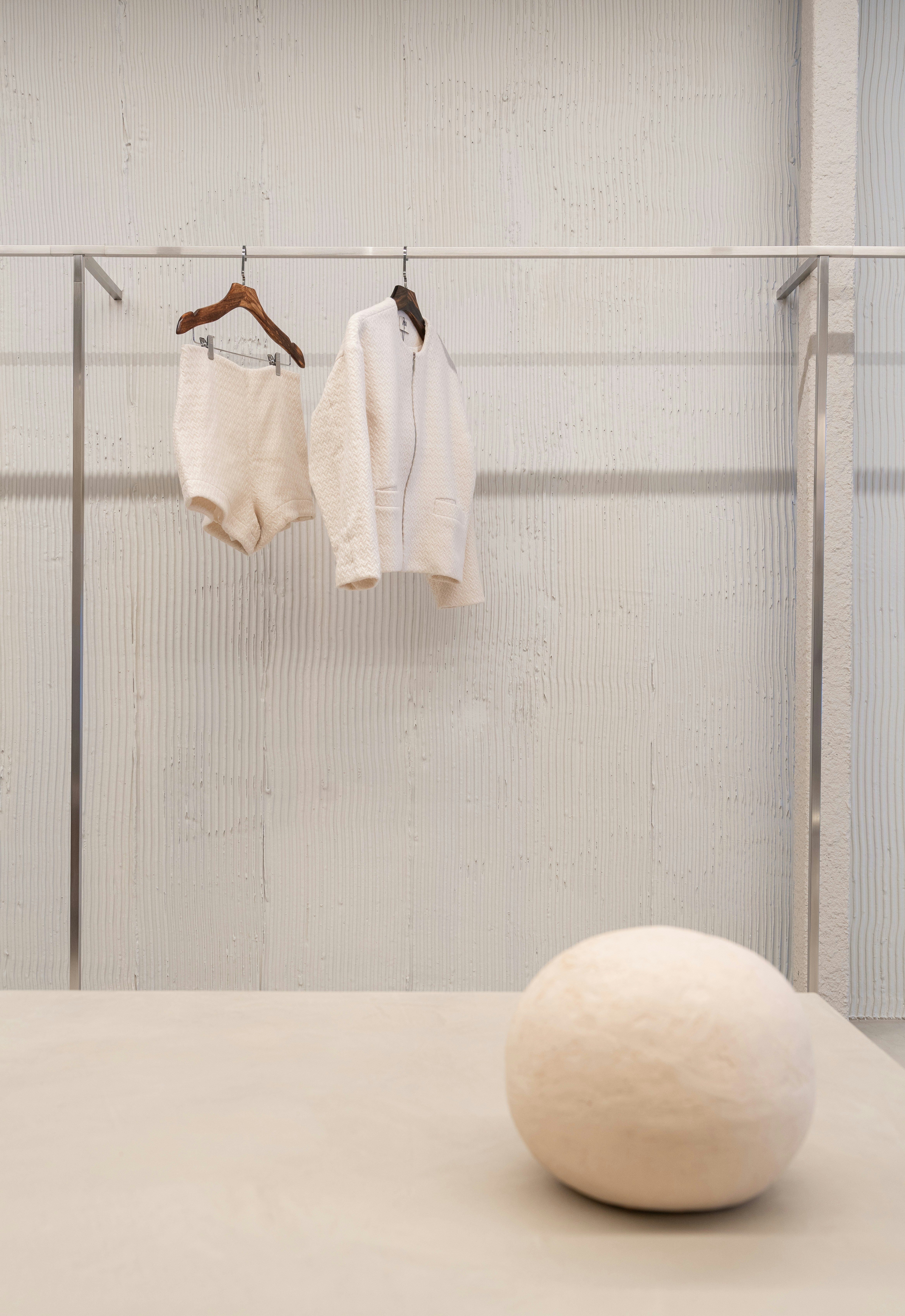 A cream jacket and shorts on hangers against a textured white wall
