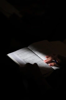 A person holding a pen over an open book of sheet music in dim light