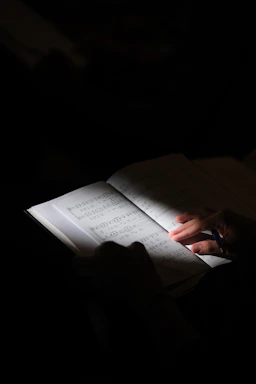 A person holding a pen over an open book of sheet music in dim light