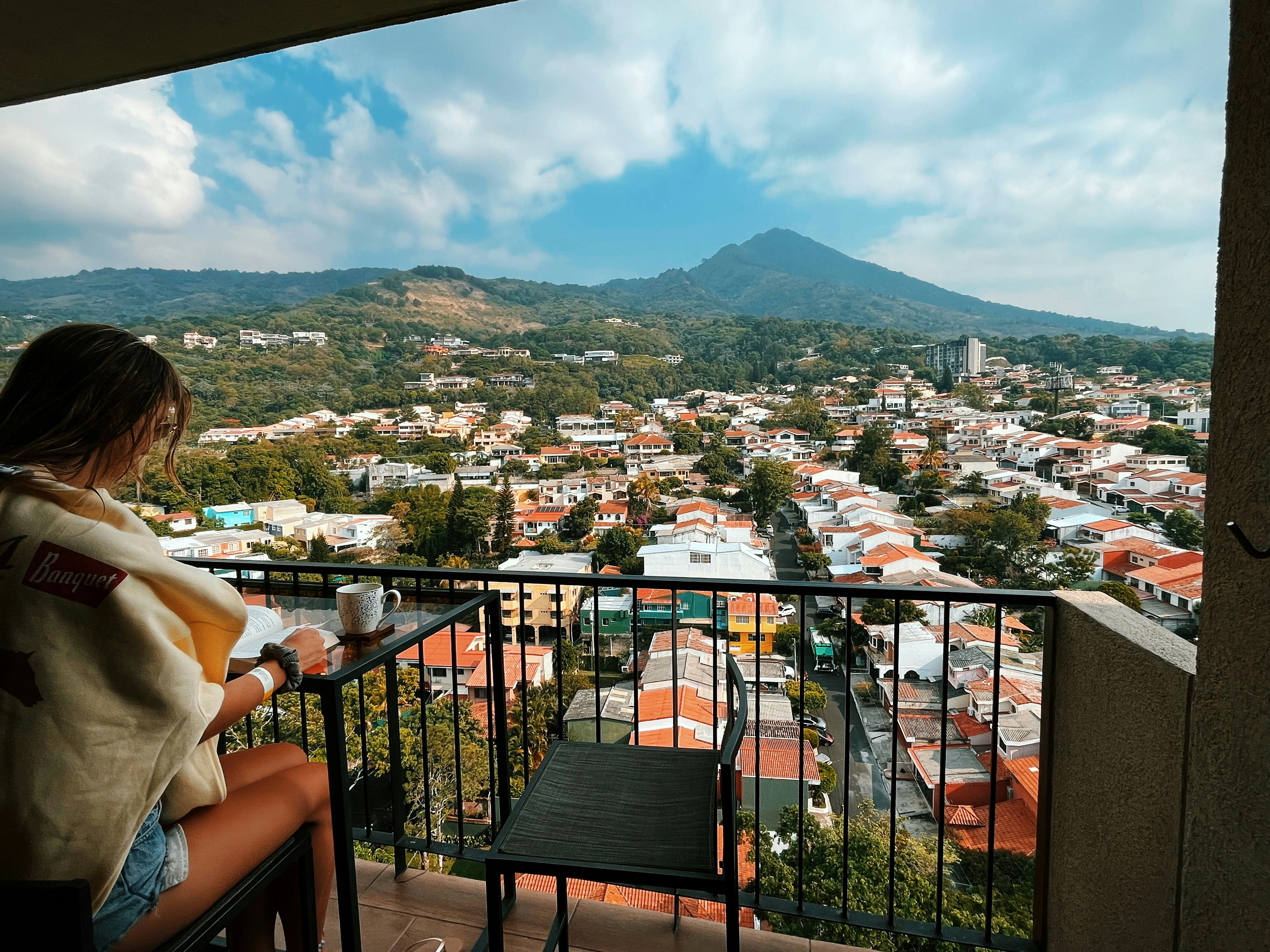 A person reading a book on a balcony overlooking a town and mountain