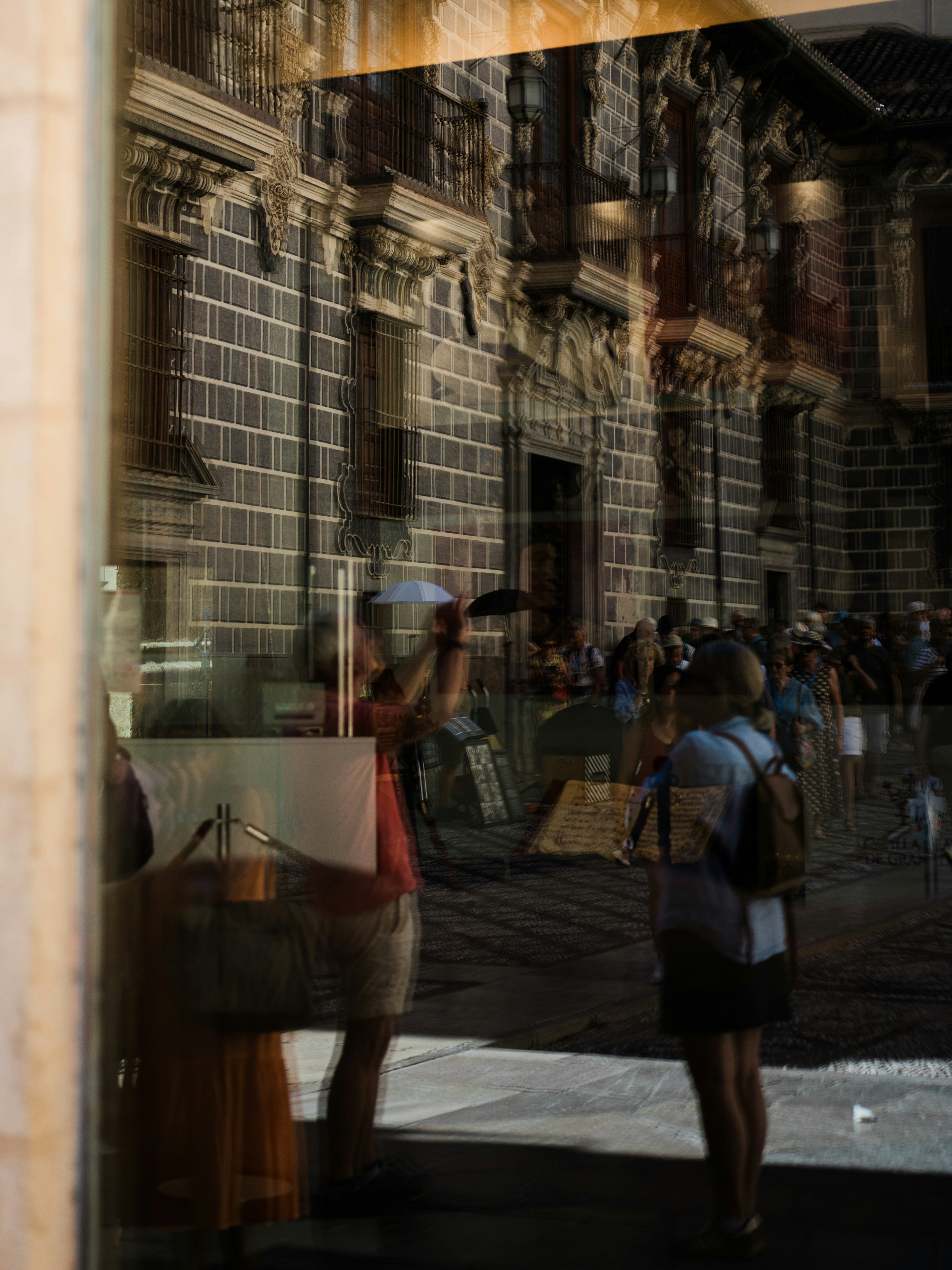 Reflections of people and a historic stone building on a glass window surface