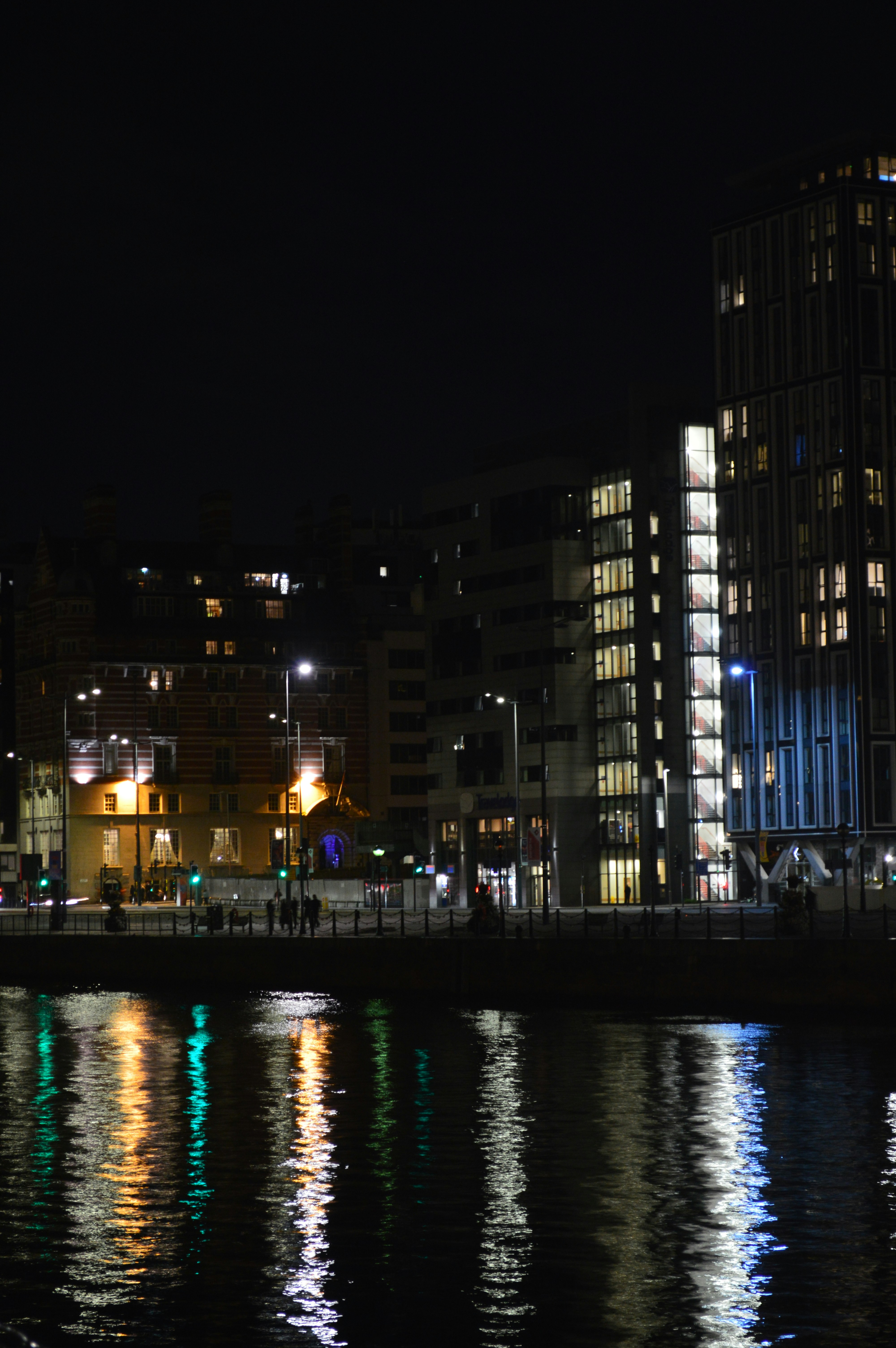 City buildings at night with glowing windows reflected in dark river water