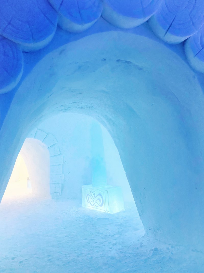 Interior of a carved ice corridor lit deep blue, with arched walls cut from solid ice