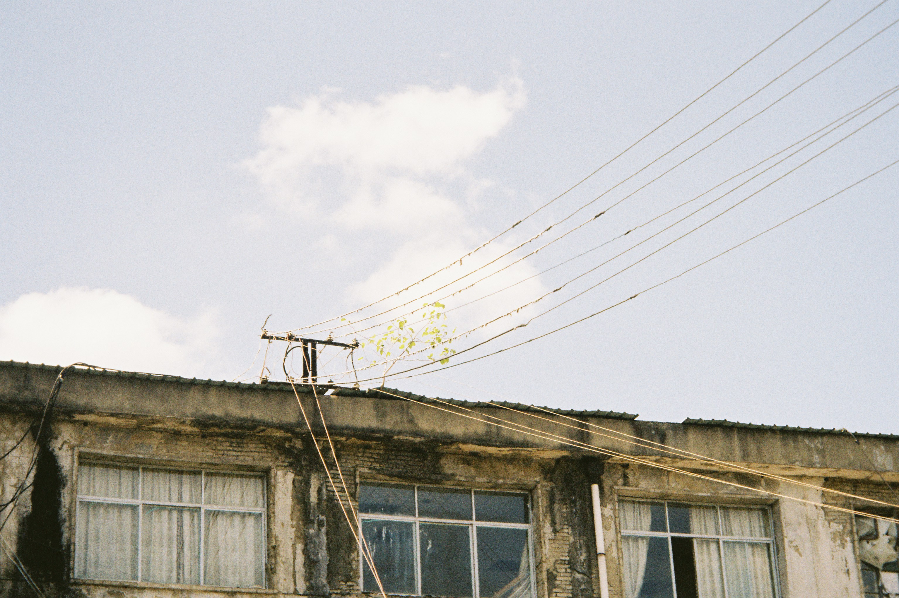 Power lines stretching from a weathered building roof against a pale blue sky