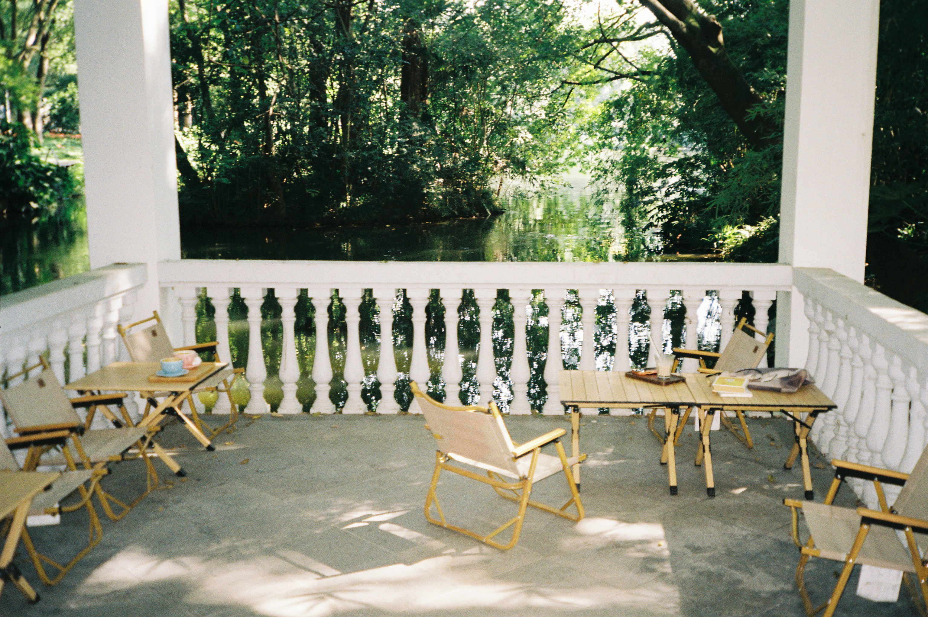 Folding chairs and tables on a stone terrace overlooking a pond and trees